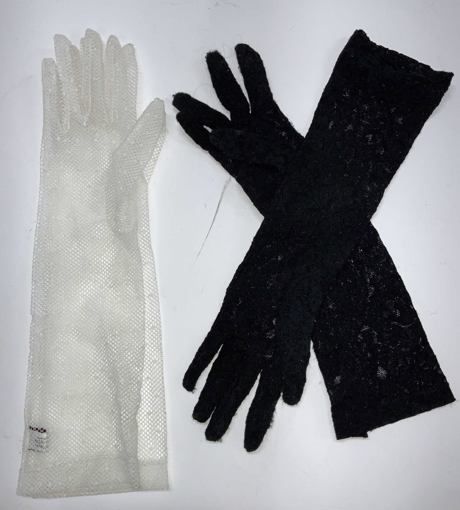 SERMONETA Black & White Cotton Driving Gloves: 2 pairs of SERMONETA driving gloves. 1 black pair with floral motifs. And 1 white pair made of fish nets. Tags white gloves are marked SERMONETA gloves, 100% Cotton. Black gloves are marked 80% Viscos