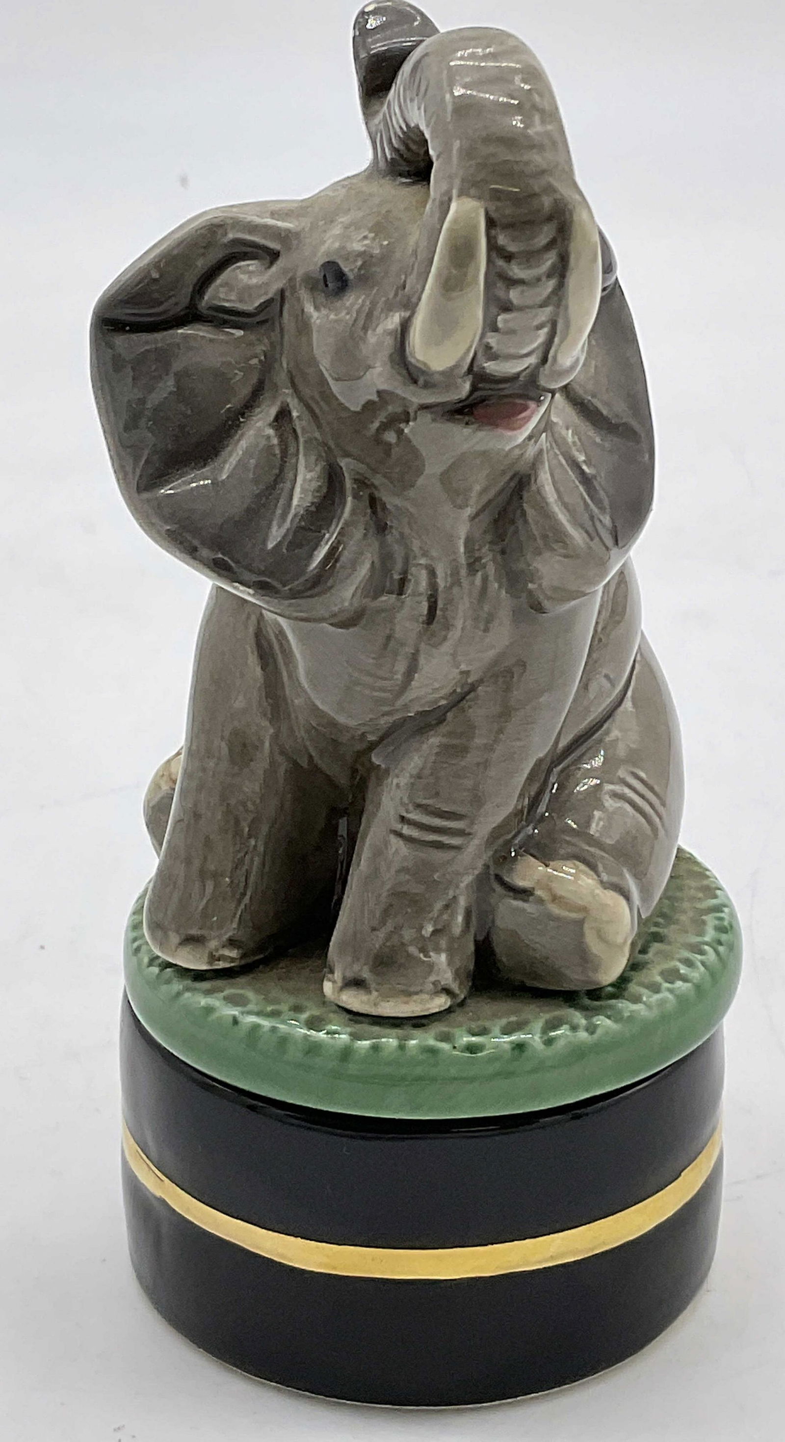 Porcelain Seated Elephant Pill Box: Porcelain Seated Elephant Trinket Box. Bottom part has a gilt line. Elephant seated on top of green lid. Two part piece. Measures approx 2W x 5H inches. Small chips present and surface wear. Elephant