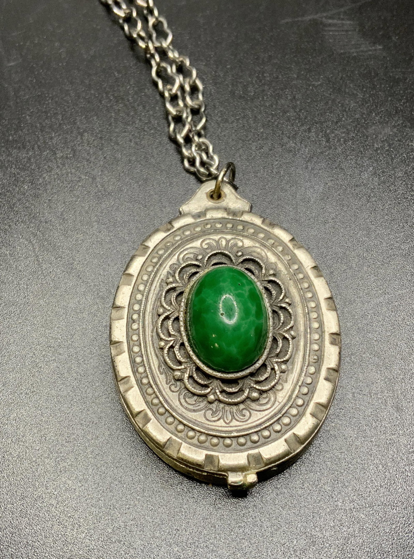 Pewter Locket w Inlaid Ornamentation: Pewter locket, possibly vintage. Decorated with an inlaid stone, possibly glass. Interior decorated with cast scrolling pattern, underside decorated with web like scrolling patterns. Loss to chain, re