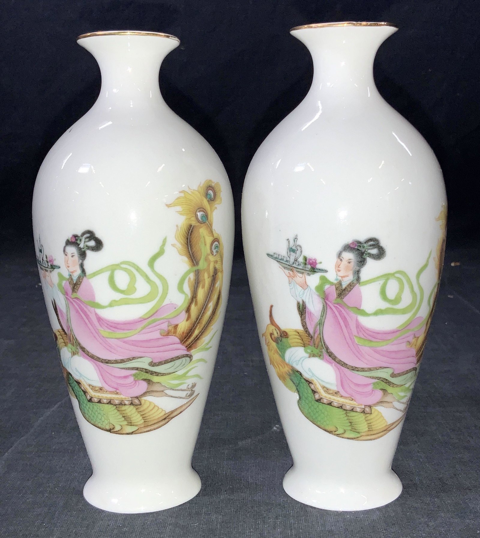 Asian Painted Porcelain Vases: A pair of asian vases, white porcelain, gold gilt rims and painted on exterior of a depiction of a woman in traditional Chinese robes seated on a peacock and holding a tray with a tea set. Marked on u