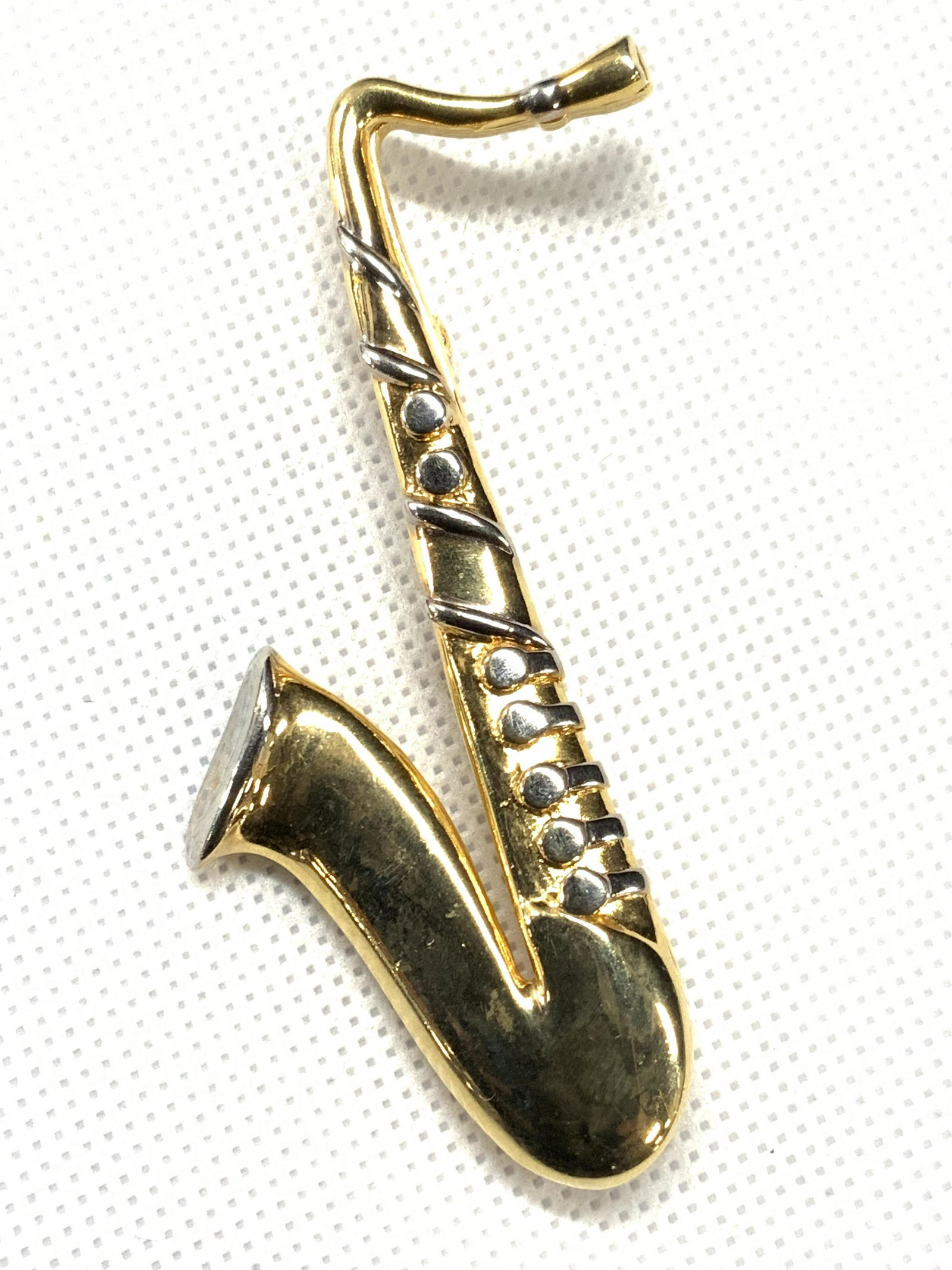 DD Signed Gold Toned Saxophone Brooch: A gold toned brooch in the shape of a saxophone, with silver toned accents. Marked DD on backside. Approximately 3 inches long. DD Signed Accessories, DD Brooch, Saxophone brooch, Saxophone, Instrumen