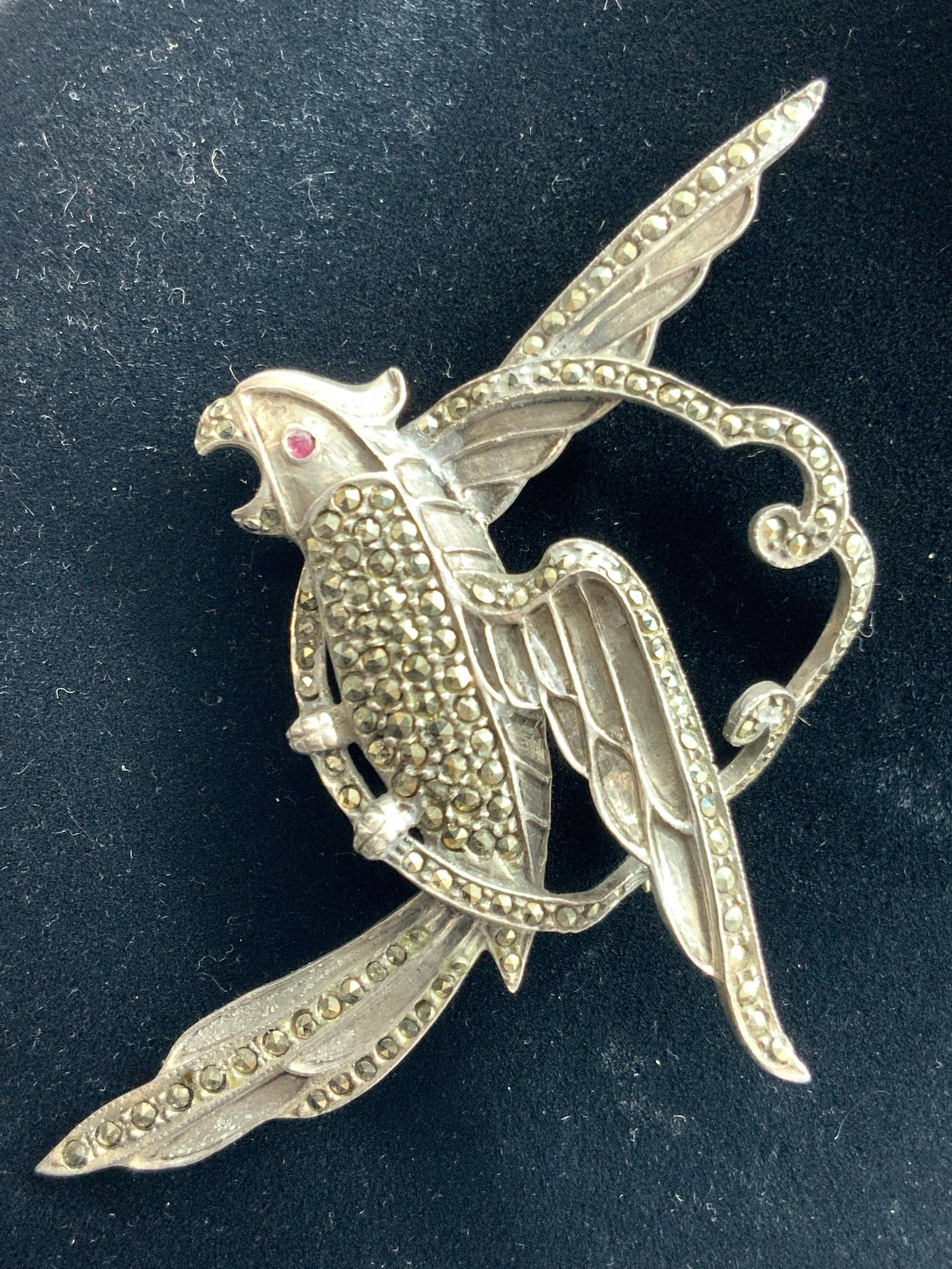 Sterling Silver Parrot Brooch: Sterling silver brooch that resembles a perched parrot, encrusted with faceted Marcasite and a red Spinel as the parrots eye. Marked Sterling on backside. Approximately 4 inches long and 2.5 inches wi