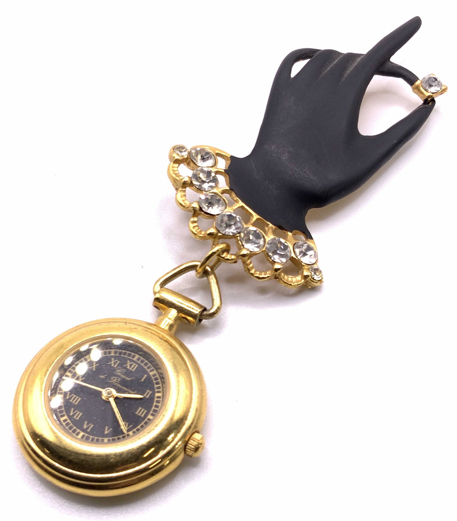 GERARD DE REAUMONT Vintage Hand Form Watch Brooch: A metal brooch crafted to resemble a hand. The hand has a matte black finish and open metalwork towards the base. Faceted crystals stud the open metalwork. Affixed to the hand via bail is a gold tone 