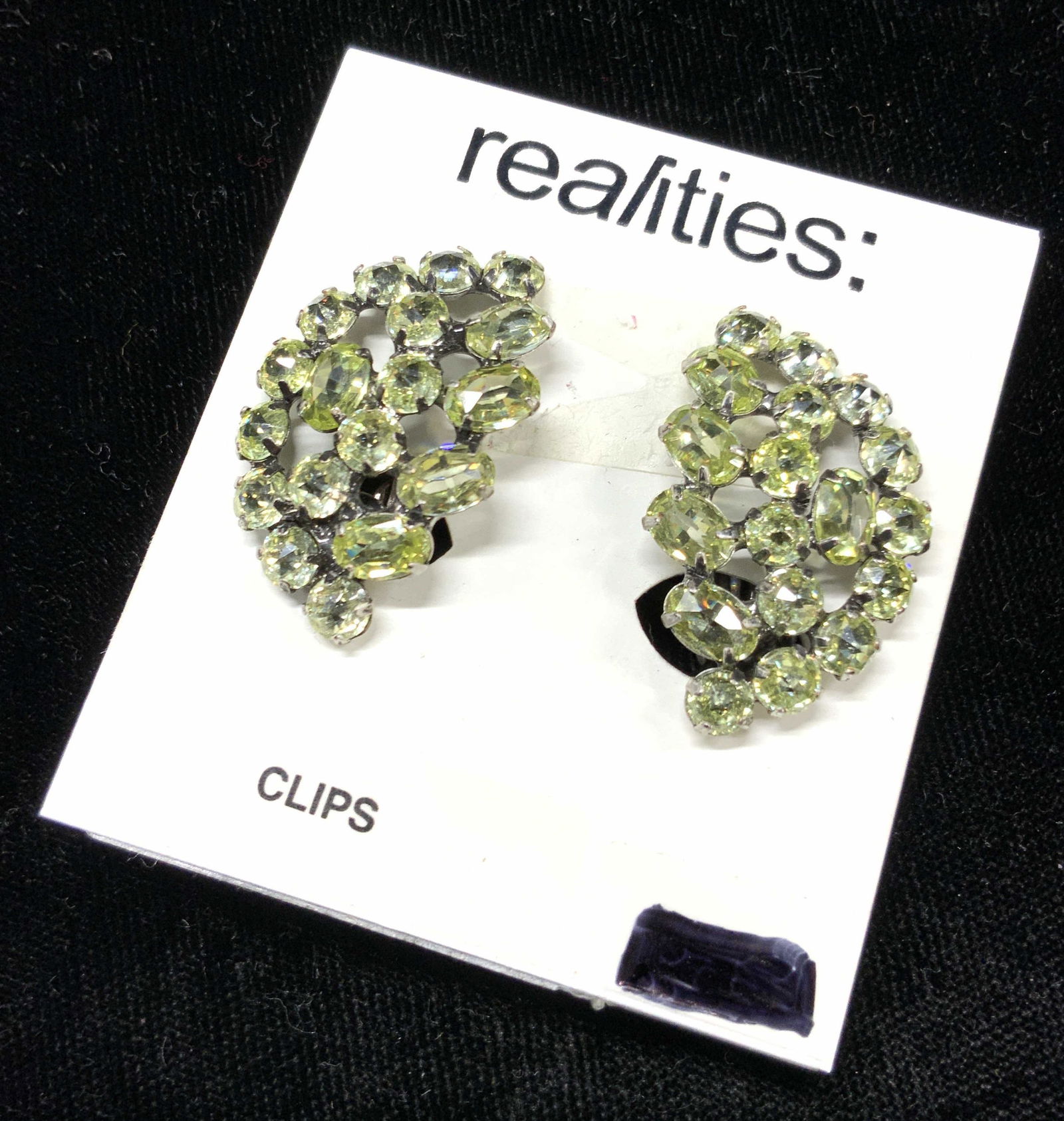 REALITIES Cluster Clip on Earrings: Pair of clip on earrings with clusters of fetched green toned crystals in leaf shape designs. Comes on display card marked Realities. Approximately 1.25 inches long. Realities clip on earrings, clip o