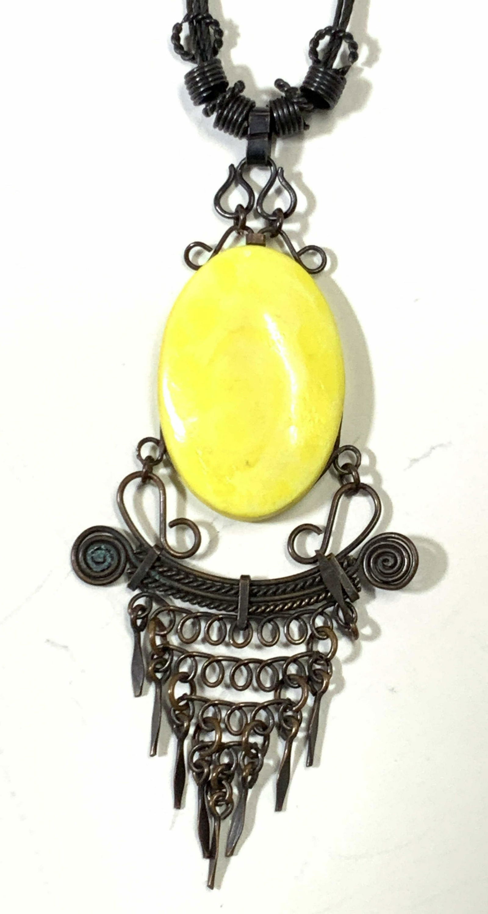 Ornate Copper Necklace, Jewelry: A necklace made with a yellow plaster made pendant, connected to an intricate copper metal design that hangs below the stone, connected with a web of spirals. A black cord runs from this to the hook c