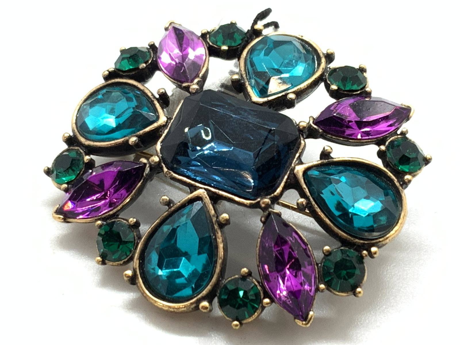 Chicos Brass Toned Blue & Purple Stone Brooch: A brass toned metal brooch with blue toned Emerald cut center stone with tear drop cut teal stones with almond shaped cut purple stones. Approximately 2.25 x 2 inches. Comes in original tag marked Chi