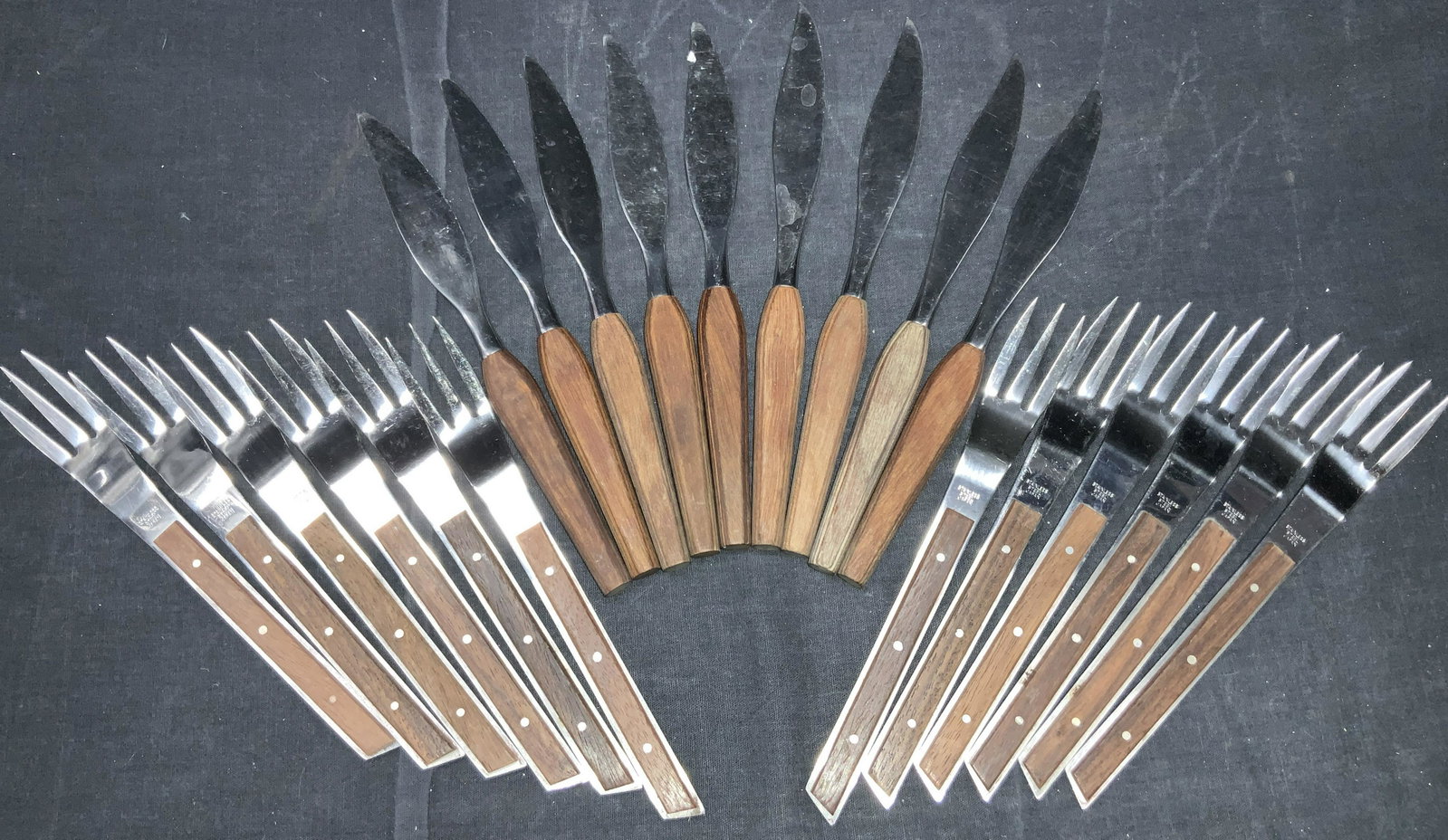 21 Stainless Steel & Wooden Silverware: Group lot of 21 stainless steel and wooden handled utensils. 12 forks marked stainless steel Japan on the steel. 9 curved bladed knives with wooden handles, possibly marked FLEETWOOD Designers, stainl