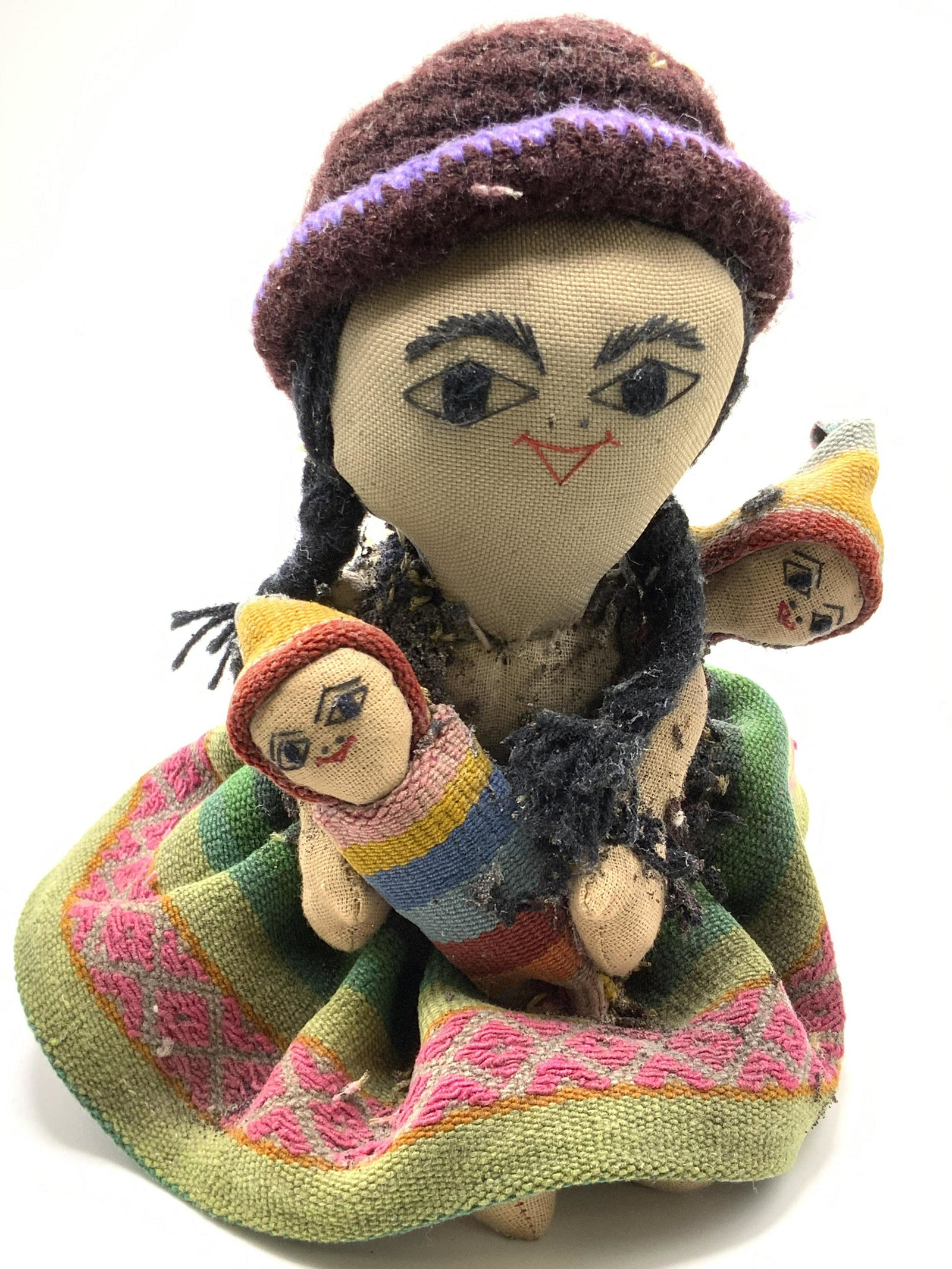 Vintage Handcrafted Fabric Stuffed Doll: A vintage handcrafted stuffed doll. Subject is a mother holding her two children. They wear colorful handcrafted clothing. Embroidered details on face. Primarily pink, red, blue, green, and earth tone
