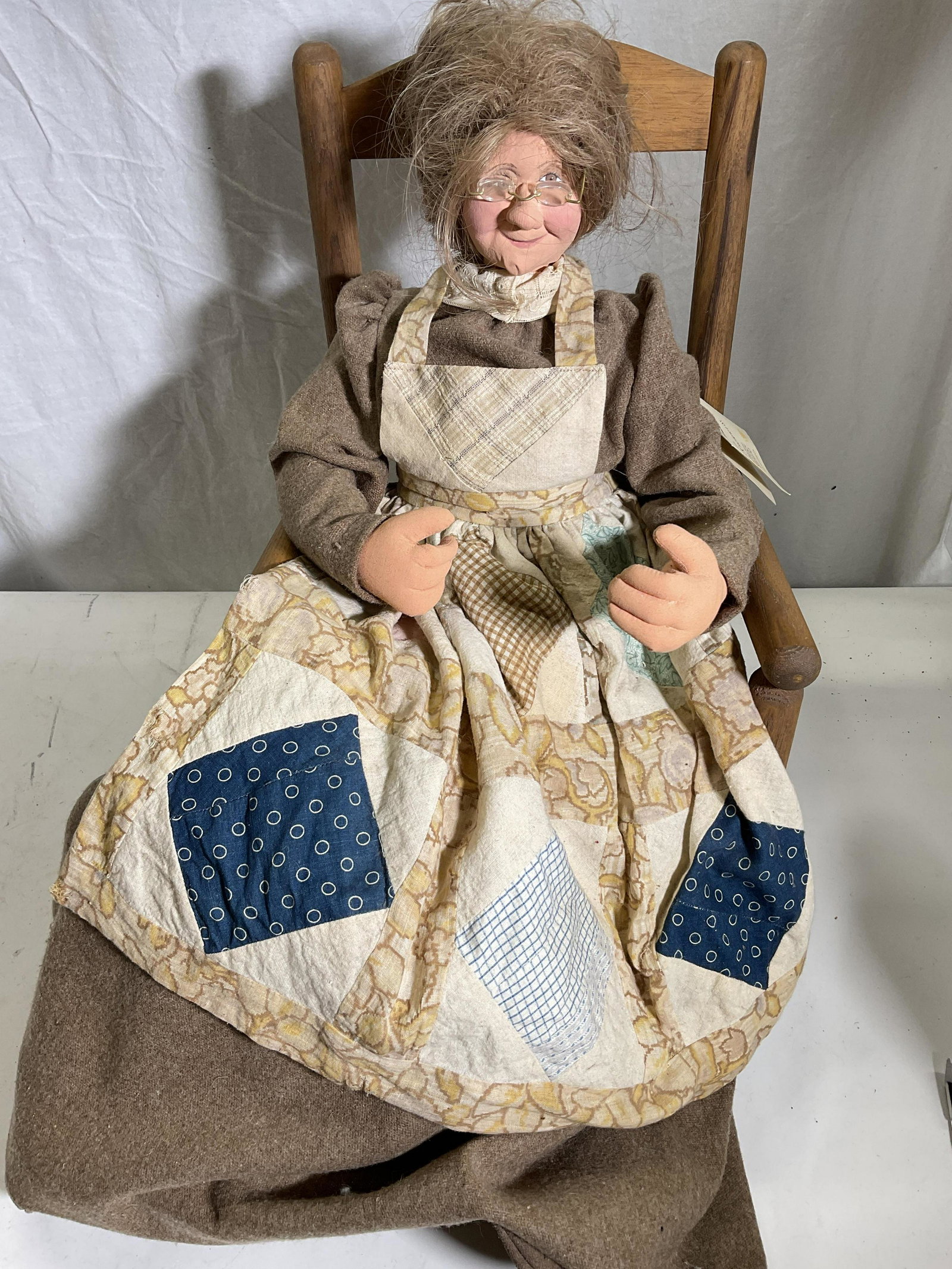 Grandma Doll On Rocking Chair: Tag on piece reads designed & made by June Weave Out of Knowwear. Her eye glasses are removable. Rocking chair is made of wood and top part is painted with flower and has a little fabric seat on top a