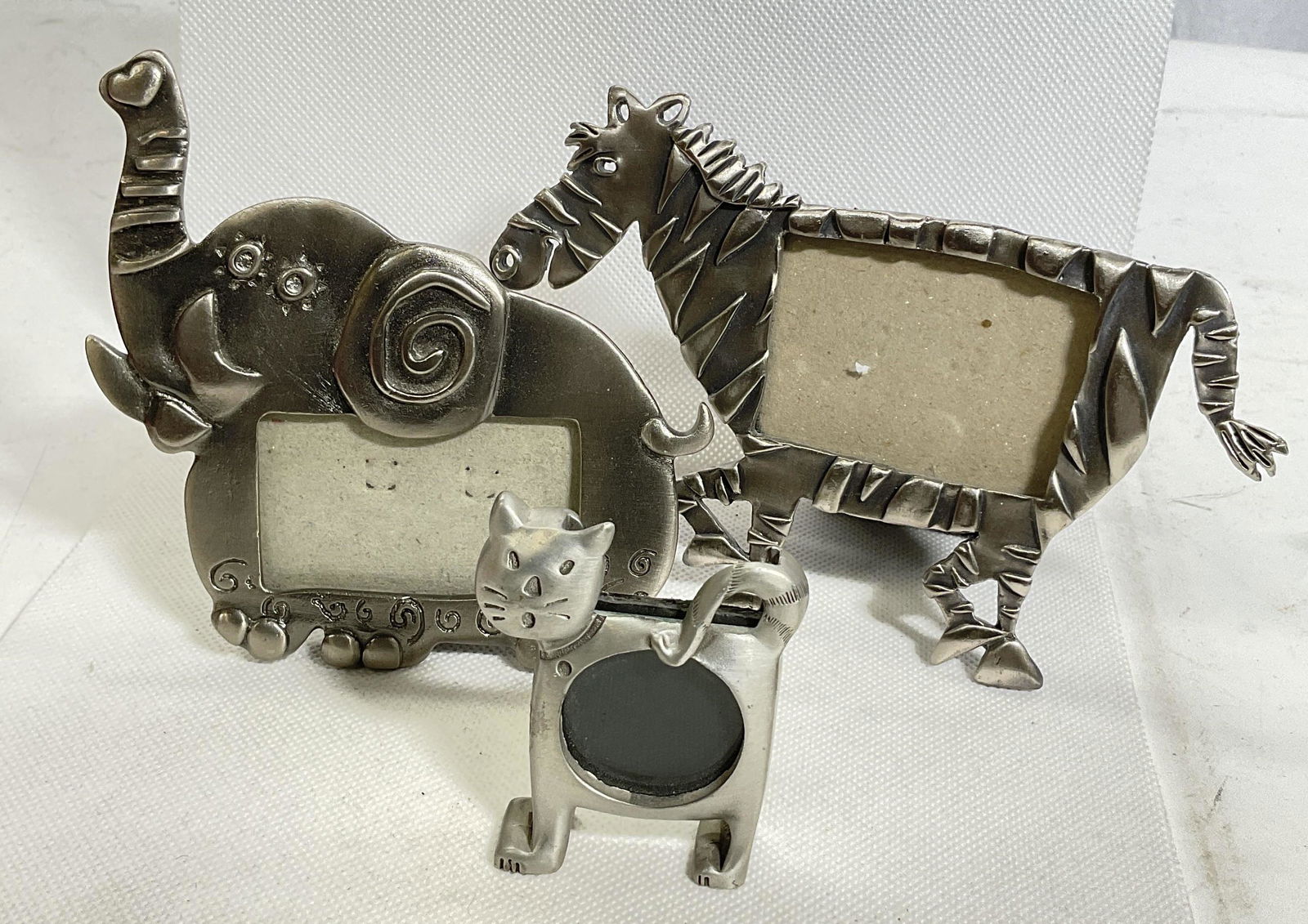 Lot 3 Animal Photo Frames: Lot of 3 metal animal photo frames. Elephant, zebra and small cat that stand up on its feet the other two are easel backs. Surface wear consistent with age and use of pieces. Largest measures 6x 4 inc