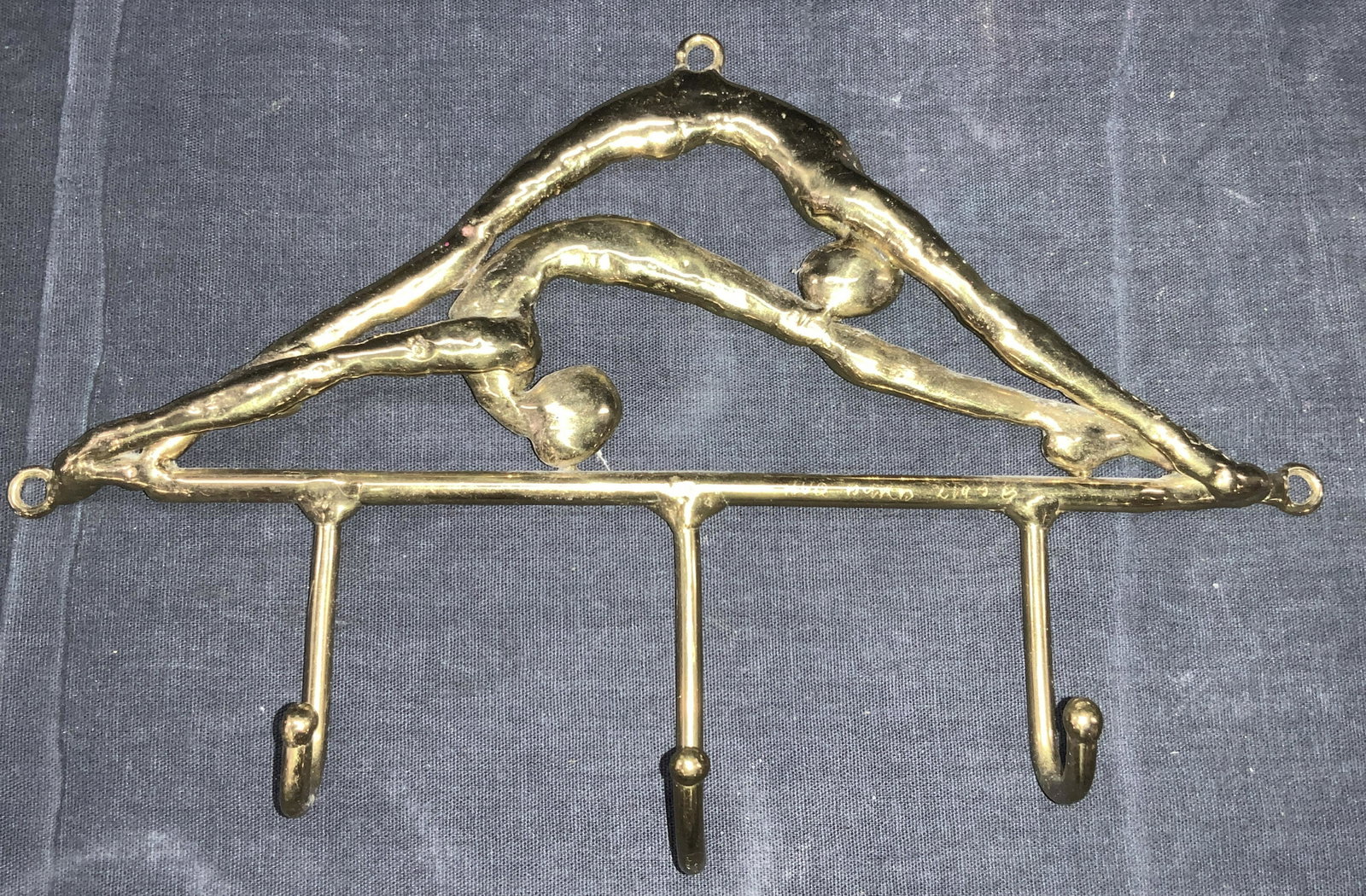 Signed Gold toned Metalwork Gymnastics Wall Hooks: A gold toned painted metalwork coat hanger with three hanging hooks. Top of hanging depicts two figures in a contoured positions arching over each other. Signed HVQ, Burd 21938. Approximately 6.25 inc