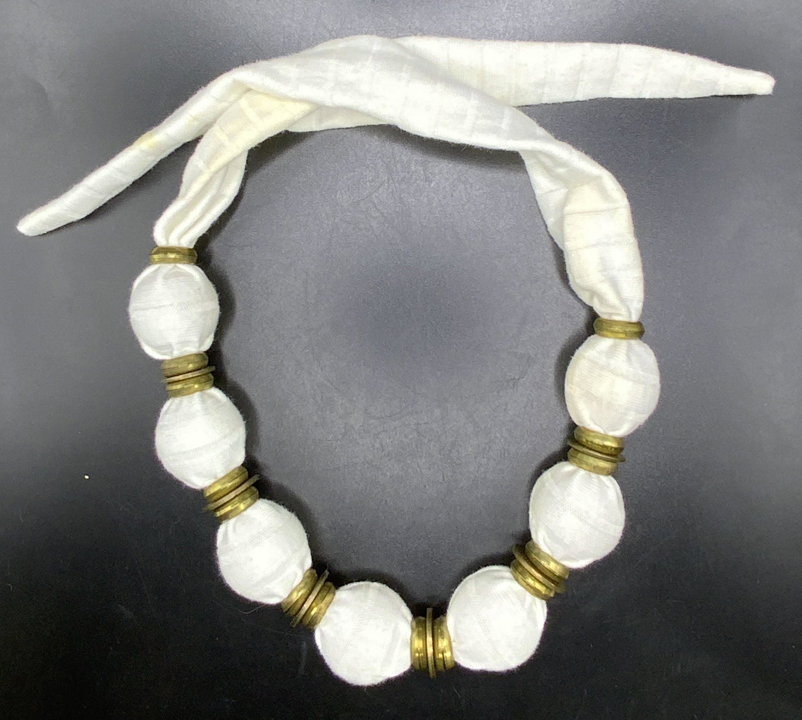 Vintage White Fabric Covered Beaded Necklace: White soft hand fabric covered beaded necklace with brass style metal hardware separating evenly spaced beads. Necklace secured by tying. Necklace measures approx. 31.5 inches long, beads measure appr