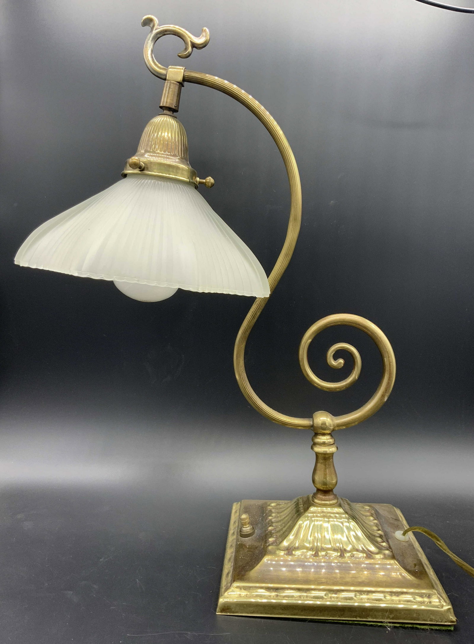 Vintage Frosted Shade Table Lamp: Table lamp is gold toned and metal. Piece has curled metal arm. Base is square shaped. Lamp has frosted glass shade. Piece measures approx 18.5 inches tall 7 inches wide 13.5 inches deep. Lamp, table