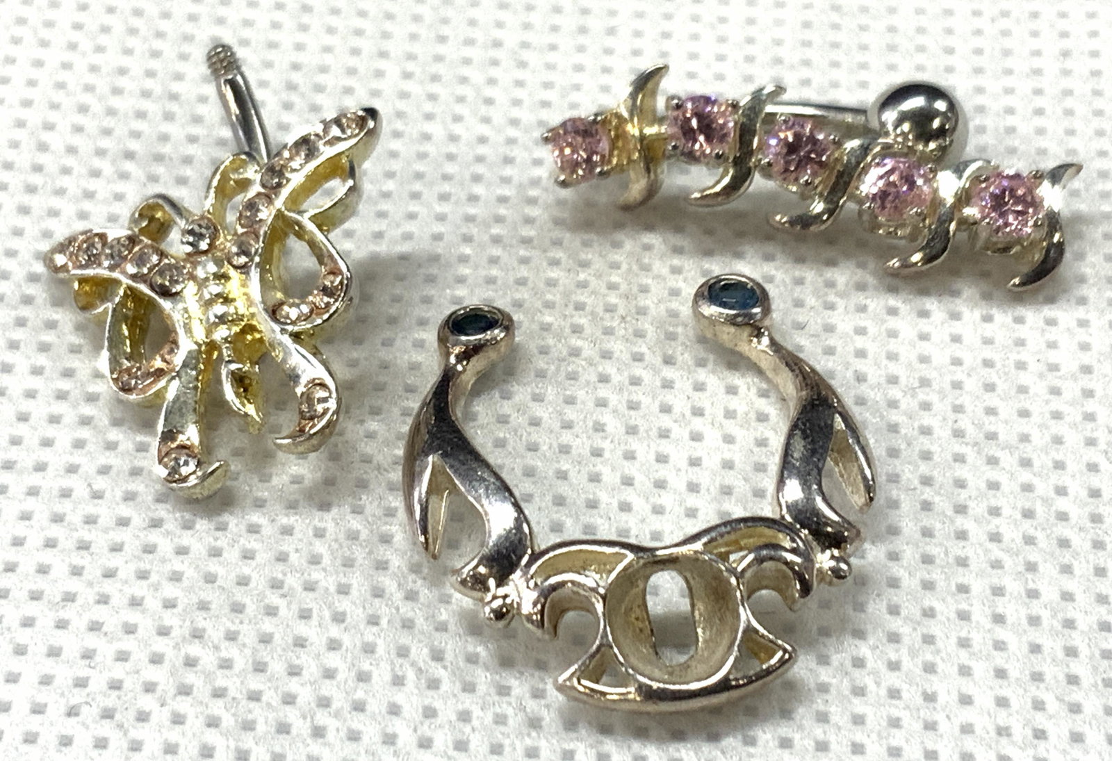 3 Sterling Body Jewelry Piercings: A group lot of 3 body piercings. 1 sterling septum ring with a missing center gem. Marked 925 on verso. Total weight 0.07 ozt. 2 belly button rings, 1 resembling a butterfly and 1 vertical piercing wi