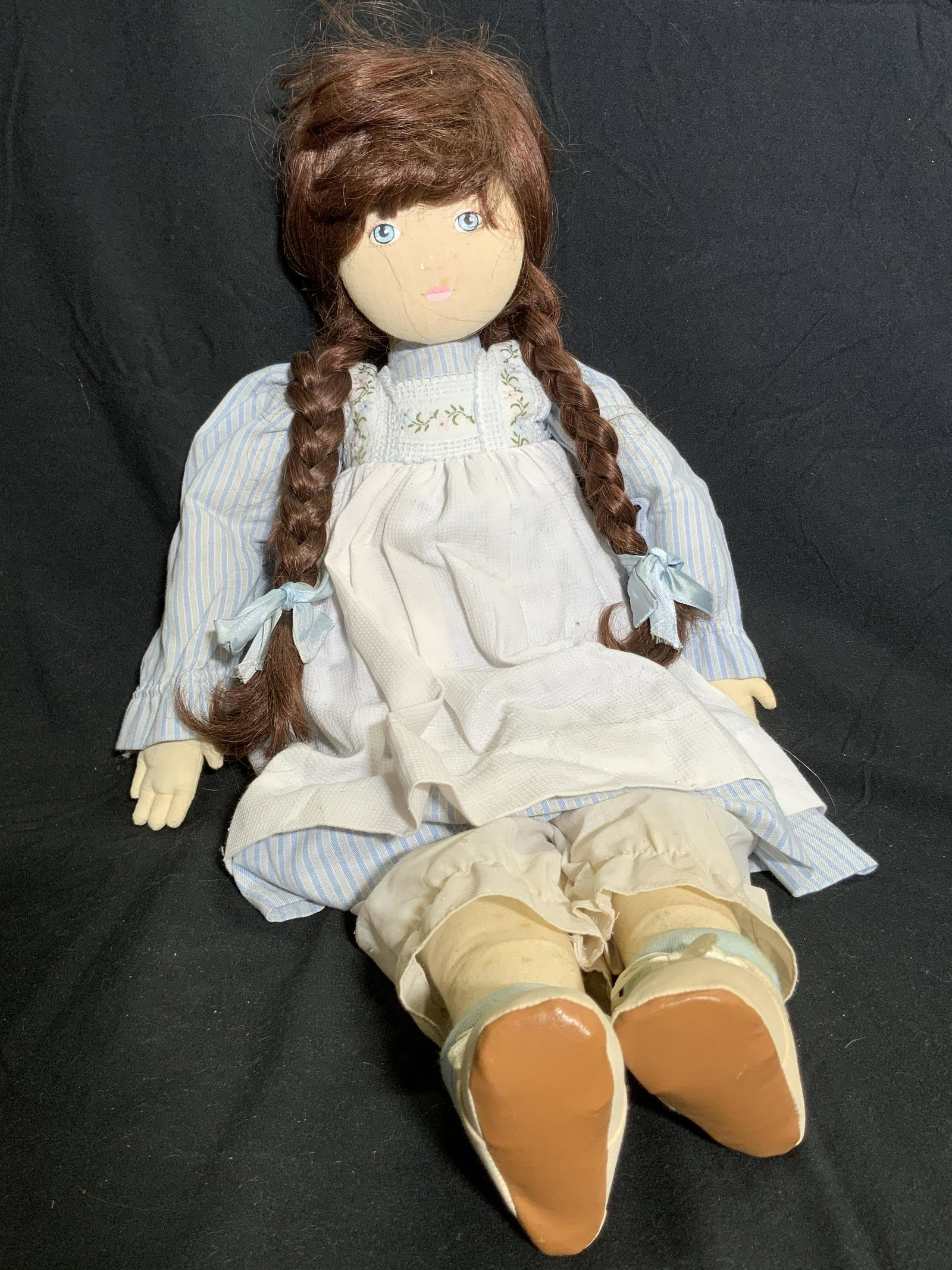 Vintage Doll W/ Brown Braided Hair & Striped Dress: A vintage doll wearing a blue striped dress with floral details. Brown braided hair. Hand decorated face. Some wear and discoloration is present. Measures approx 24L x 11W in. Dolls, display dolls, fa