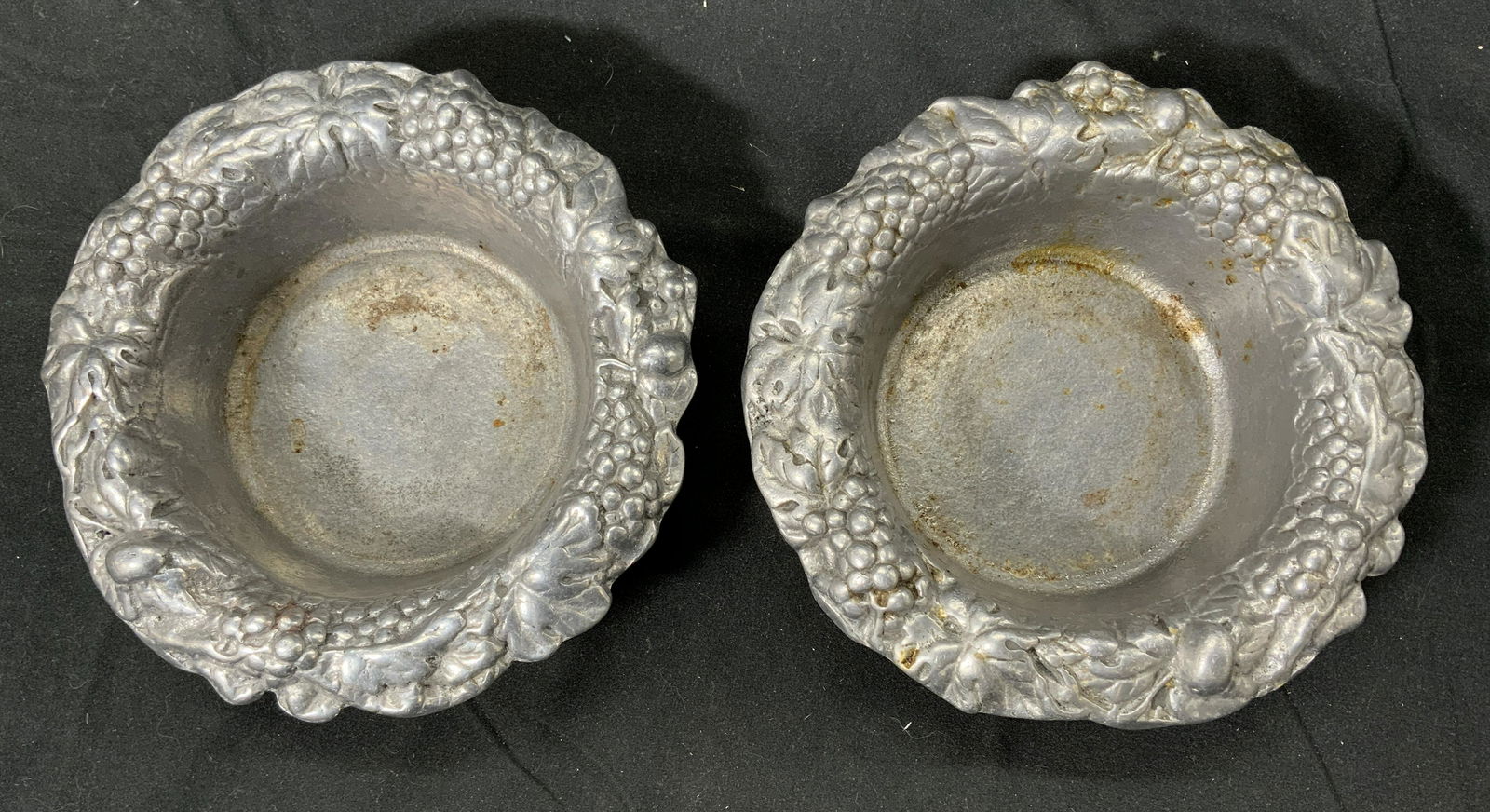 Lot 2 PELTRINA Vtg Grapevine Wine Bottle Coaster: Pair of matching PELTRINA signed vintage wine bottle coasters with grapevine motif. Cast aluminum. Good Vintage condition, needs cleaning. Signed to underside. Each measure approx. 6.25 inches wide an