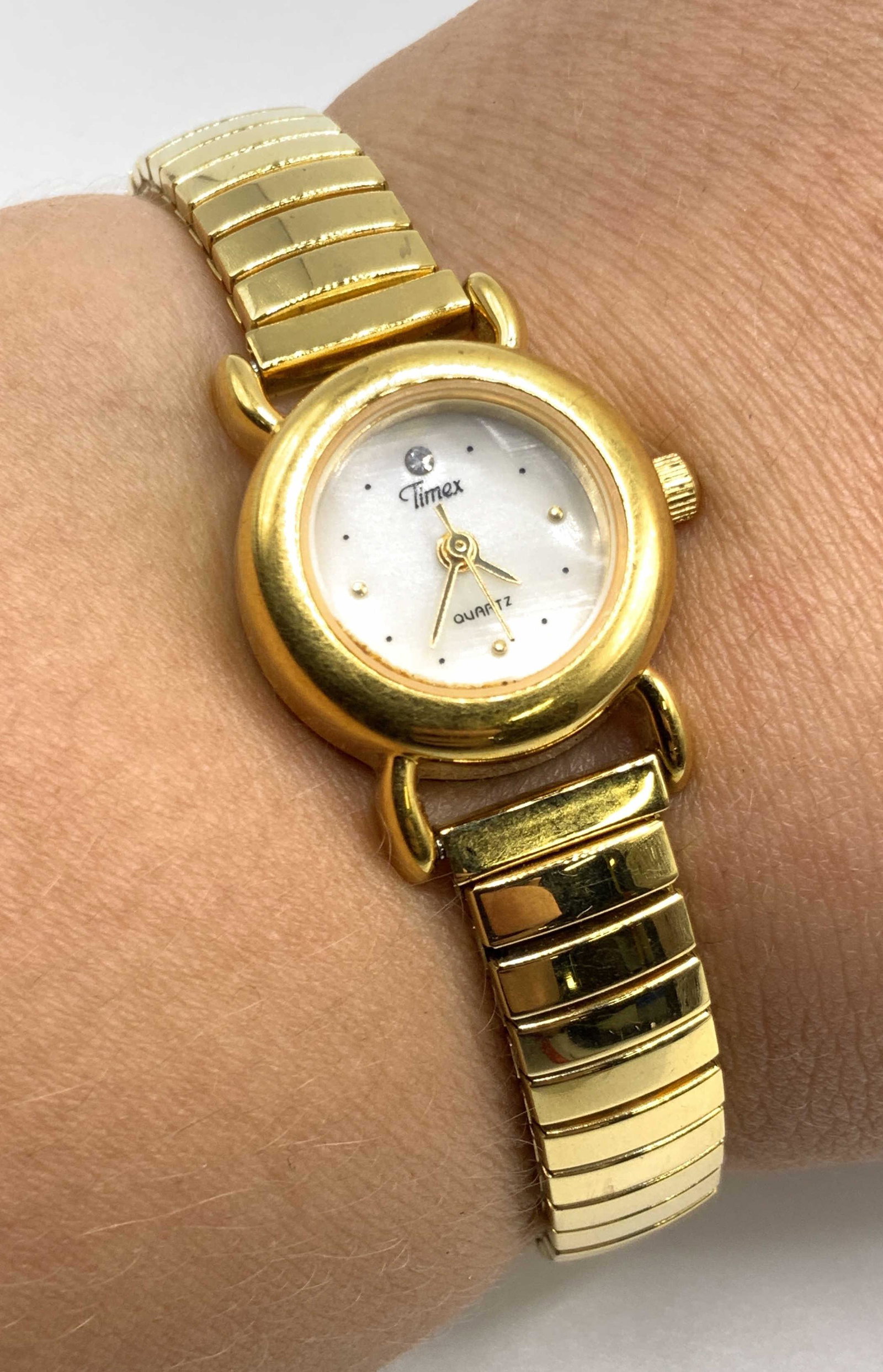 TIMEX Signed Gold Tone Stainless Steel Wristwatch: A gold tone stainless steel stretch wristwatch. Obverse reads TIMEX, Quartz. Reverse reads Stainless steel. Diameter approx 2 inches. Not tested for working condition. Some surface wear to piece. Vint
