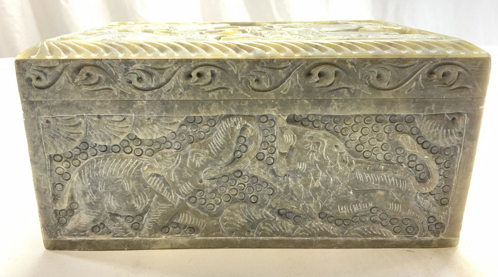 Novica Collection Carved Soapstone Keepsake Box India: Label on underside reads Novice Collection India. Keepsake box has intricately carved animal detail, carved relief figurals of lions, elephants and servants, hinged lid. Piece is slate toned and appea
