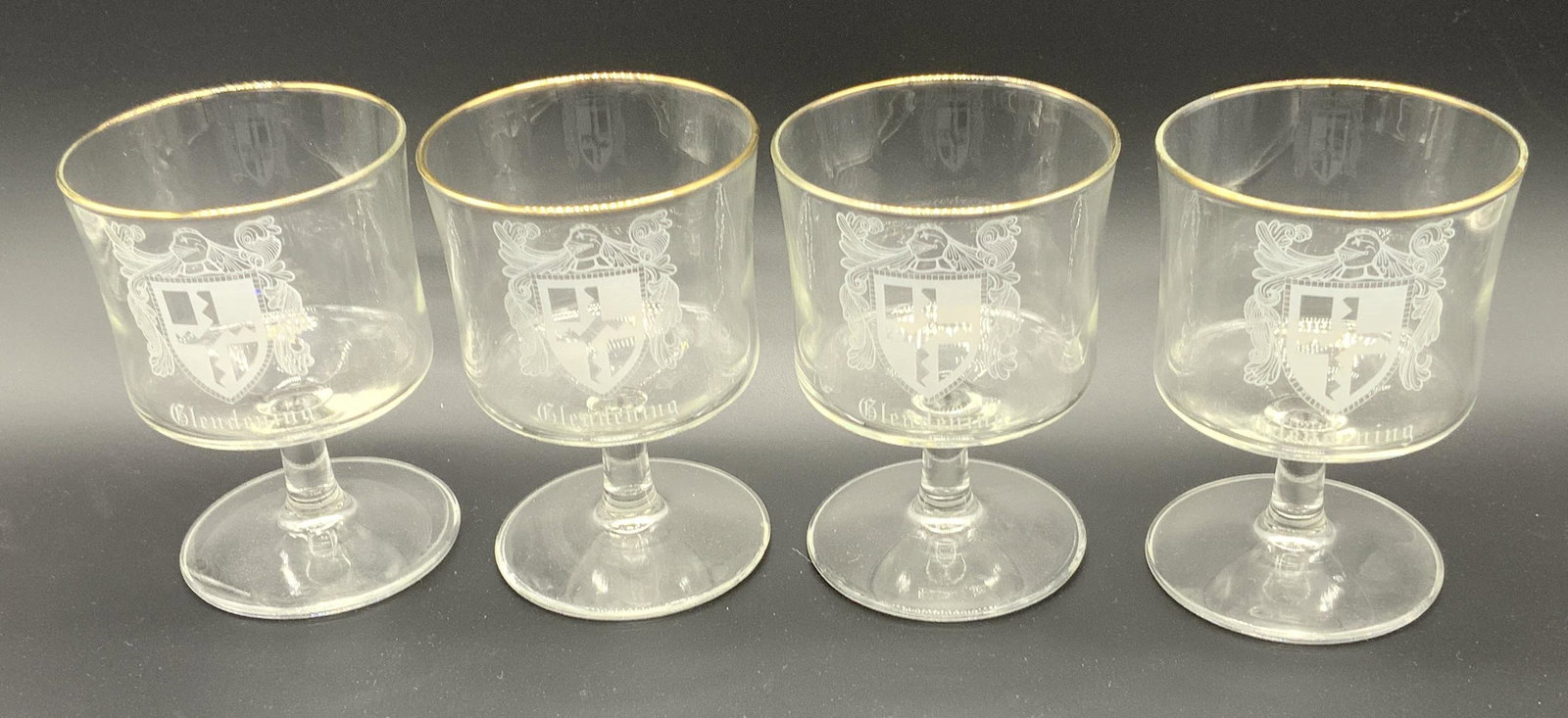 Lot 4 Gold Tone Trim Glass Goblets, Glassware: Lot of 4 clear glass goblets with gold tone trim on lip of glass and family crest motif, reads GLENDENING. Goblets measure approx. 4.25 inches in height, 3 inches diameter. Some wear to gold tone pres