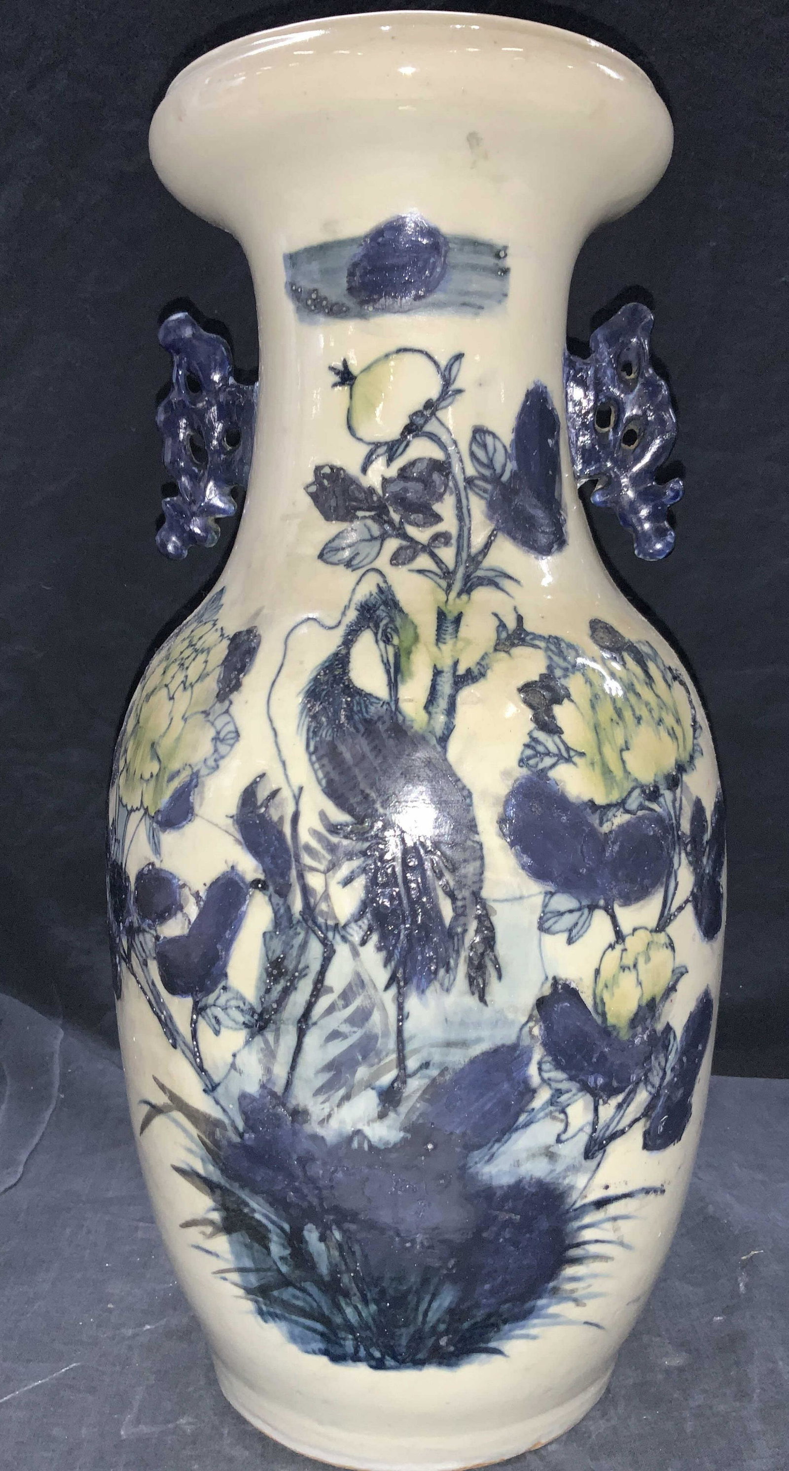 Vintage Asian Style 17 Inch Pottery Vase: A vintage pottery vase in an off white glaze, painted with dark blue and greens to depict a crane amongst flowers. Side handles on neck are blue toned. Approximately 17 inches tall. Vintage ceramics, 