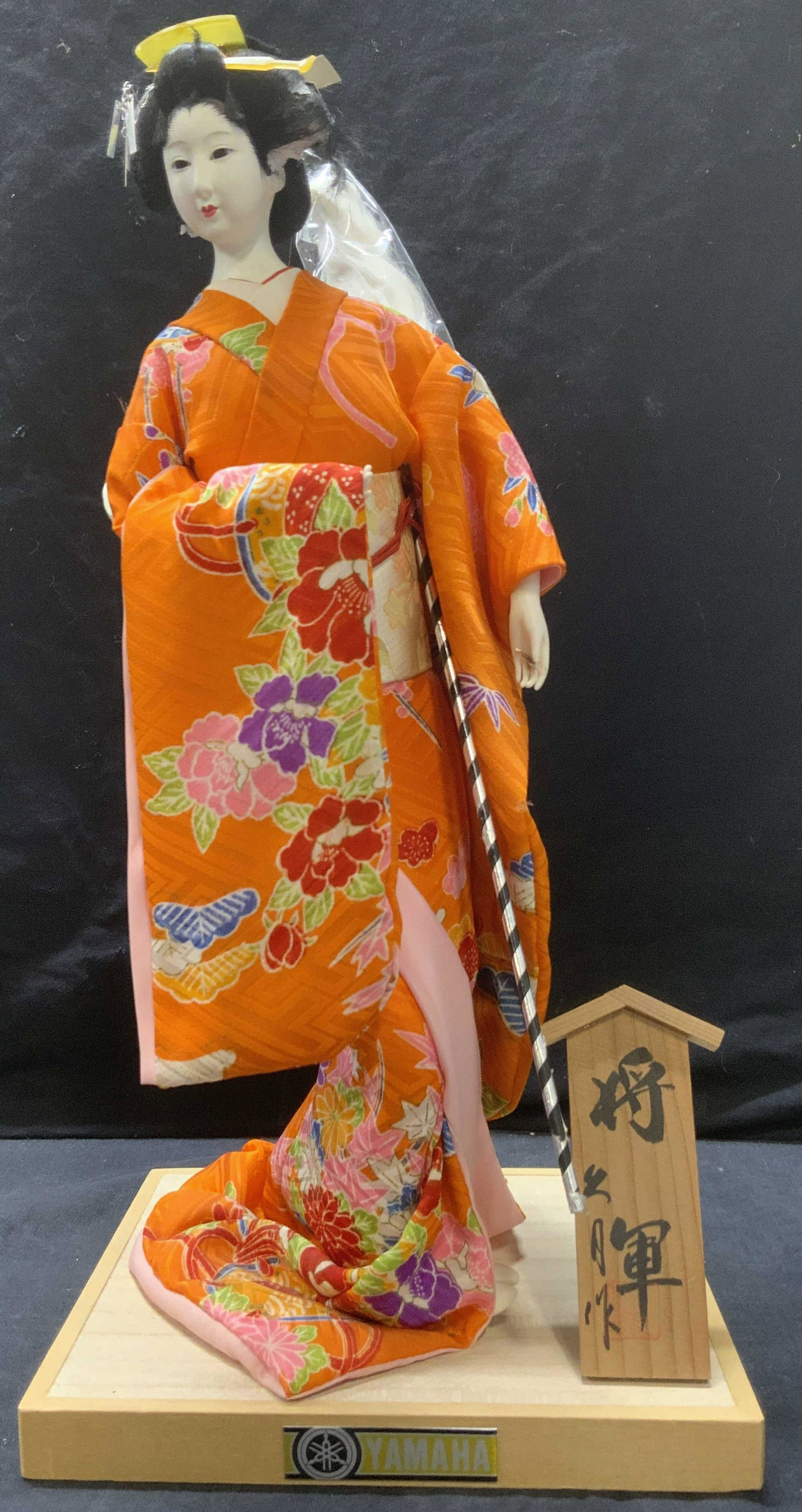 YAMAHA Kyugetsu Doll, Japan: YAMAHA Kyugetsu Doll, made in Japan, resin material mounted to wood pedestal, wearing ceremonial orange robe, with separate unattached wood plank with calligraphy. Measures approx 17 1/2 x 8 1/4 in. Y