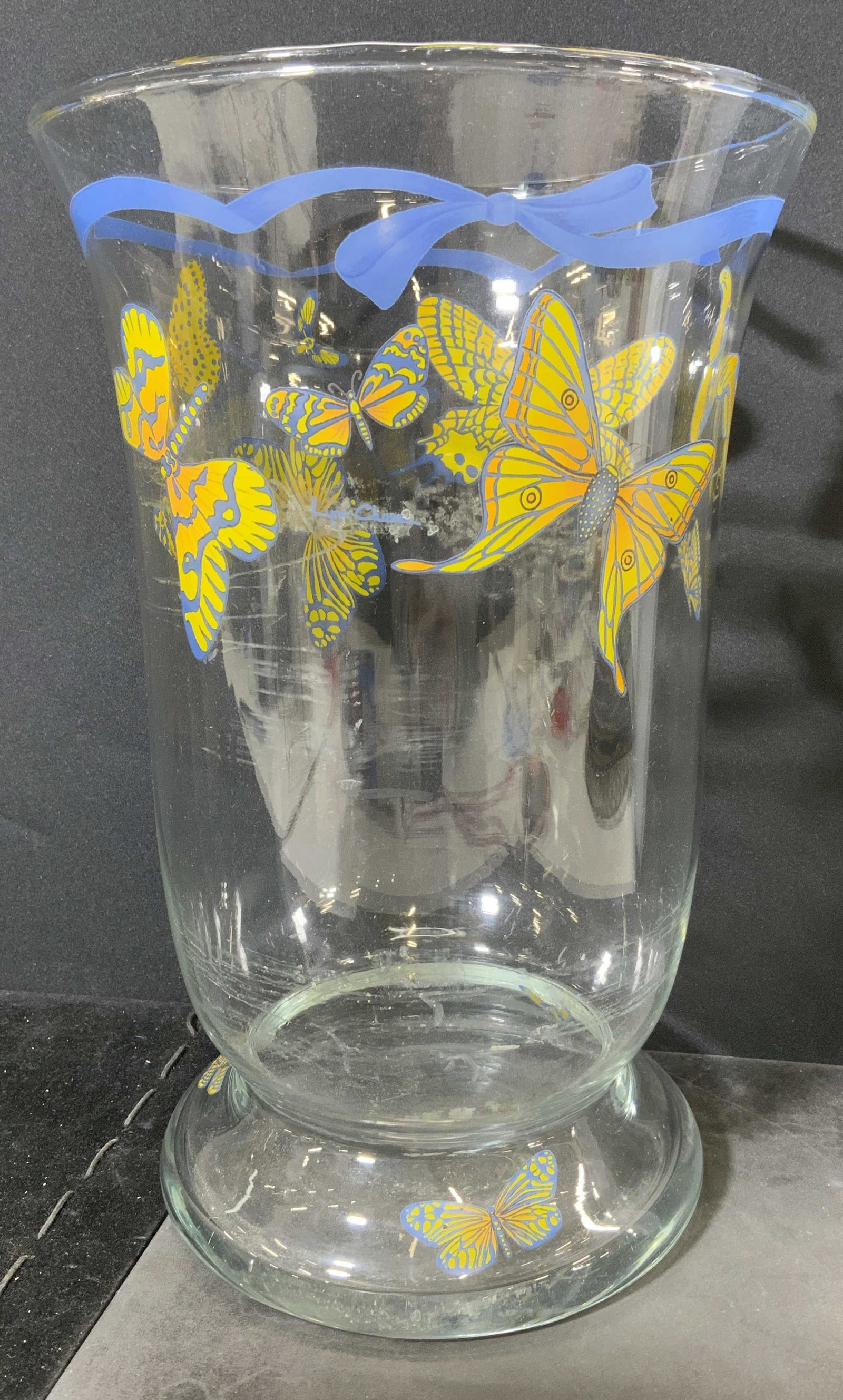 Glass Butterfly Print Vessel: Glass vessel. Decorated with prints depicting various butterflies and ribbons, signed Lynn Chase as a part of print. Surface wear and scratches present. Measures approx 12 inches h and 8 inches w. Hom
