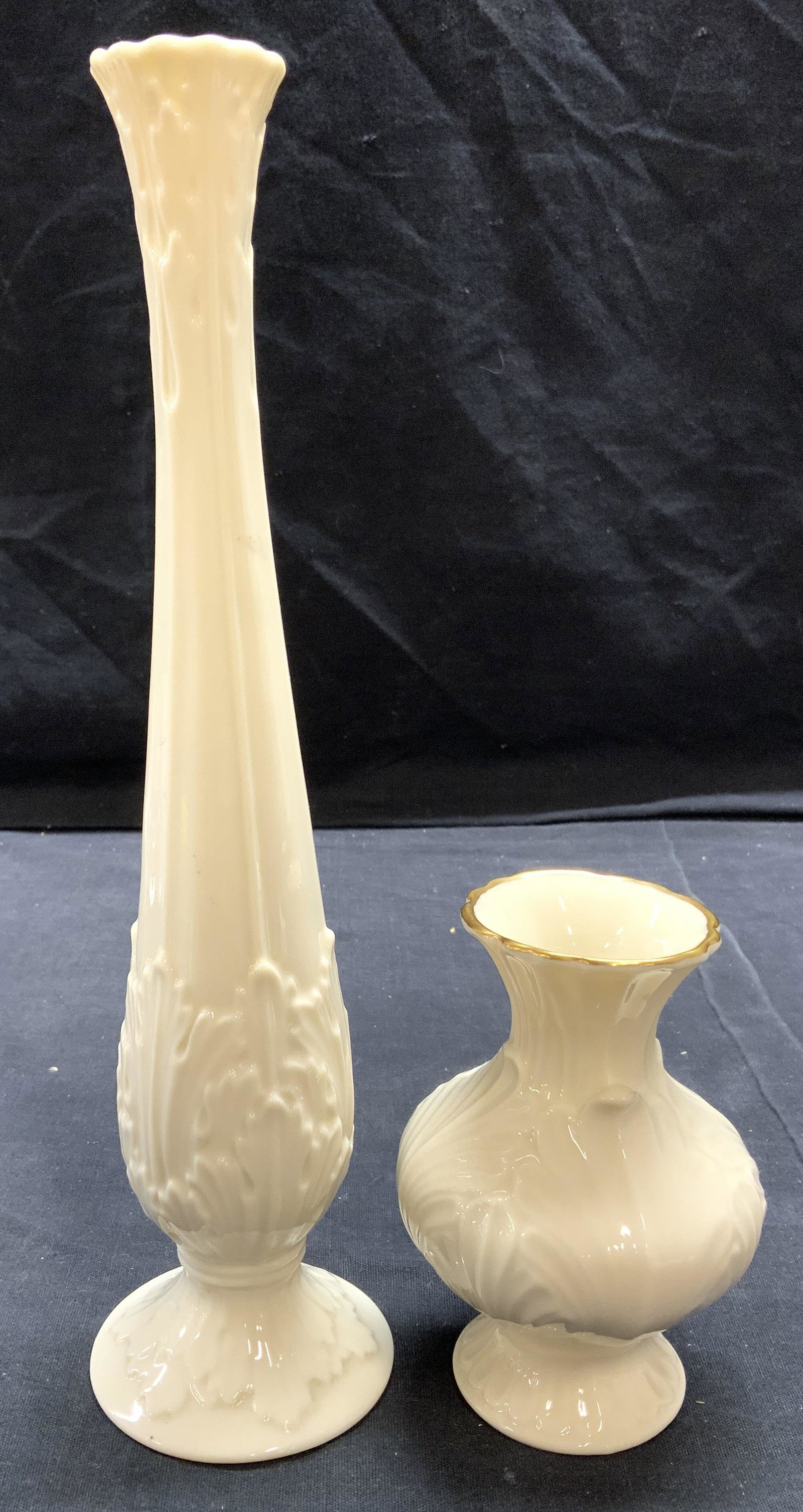 Lot 2 LENOX Porcelain Vases Vessels: Lot includes 2 vases. Each are marked LENOX MADE IN USA on underside. Each vase is footed. Shortest vase has a gold toned rim. Largest vase measures approx 10.75 inches tall 2.5 inches wide. Vases, Le