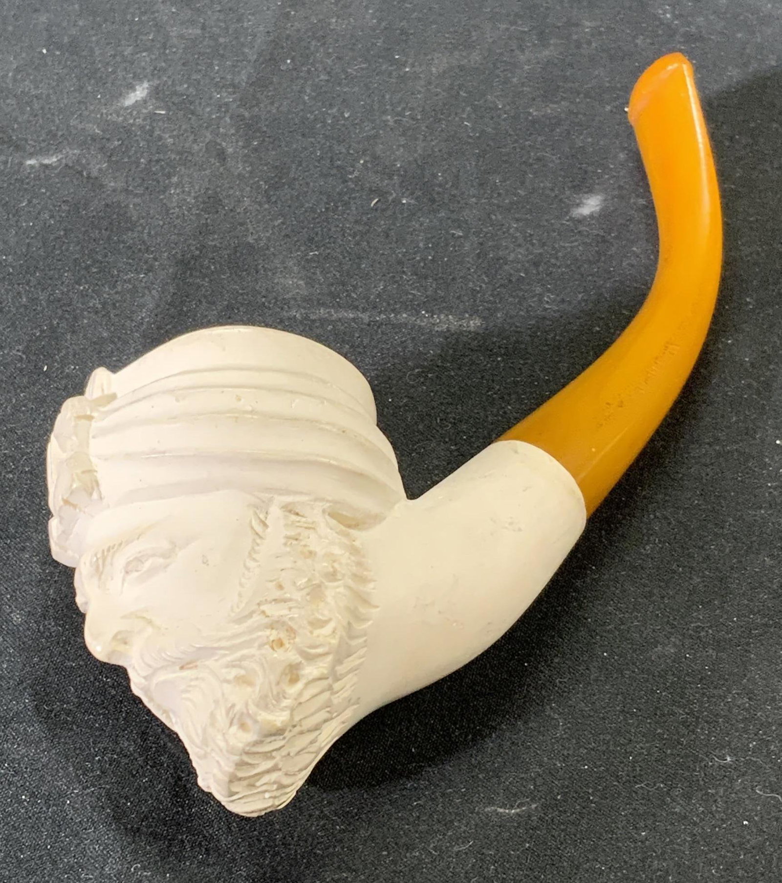 Figural Motif Decorative Tobacco Pipe: A decorative tobacco pile with figural motif. Bowl features head of a male figure. Composed of composite materials. Surface wear consistent with exposure. Measures approx. 5.5 x 1.5 x 2 inches. Pipe, 