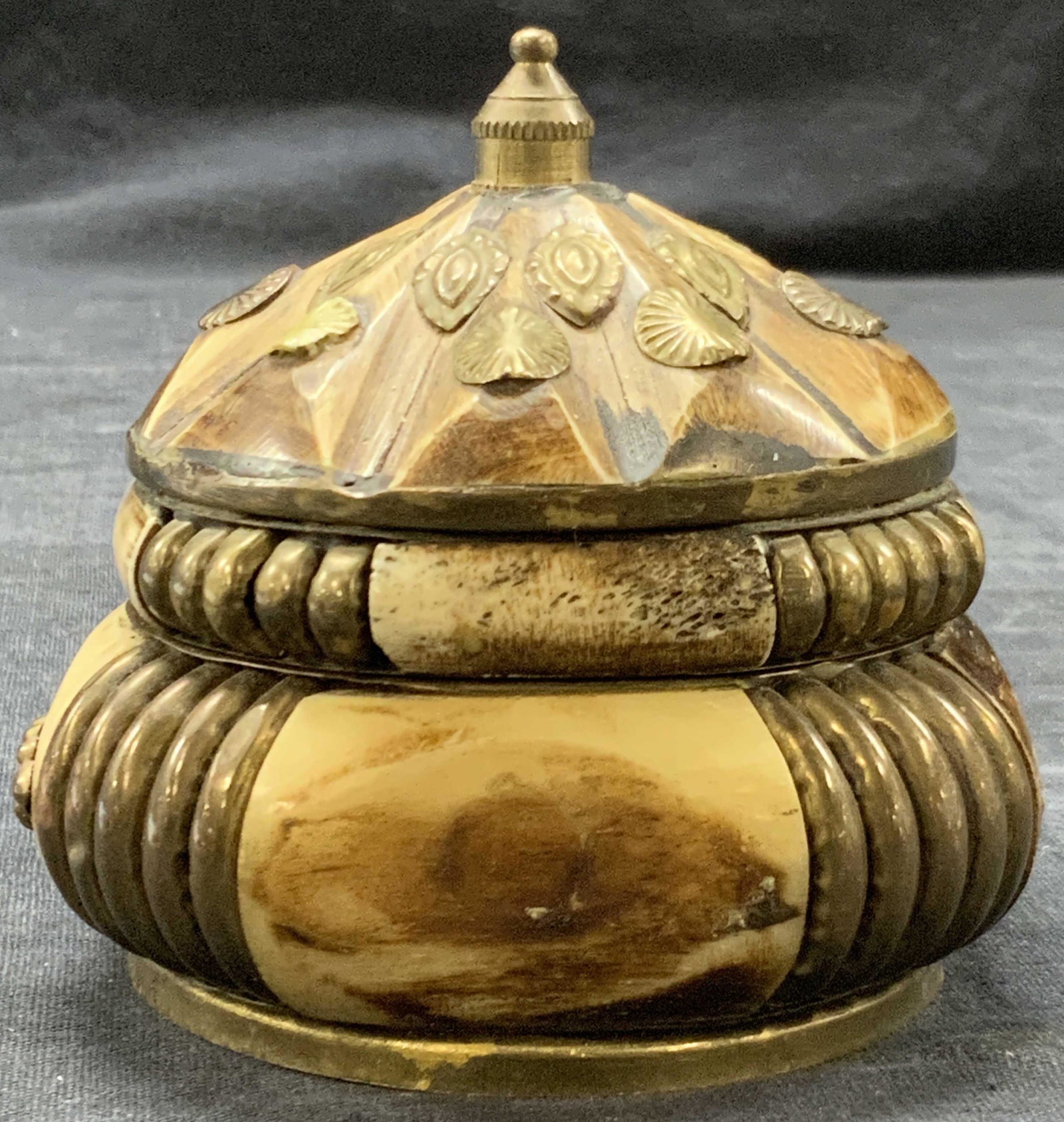 SUDHA Vintage Carved Bone & Brass Trinket Box: A vintage trinket box crafted from carved bone and brass metal inlays, with a removable lid adorn with leaf shaped decorations. Approximately 3.25 inches tall, evident loss to lid decor. Marked SUDHA 