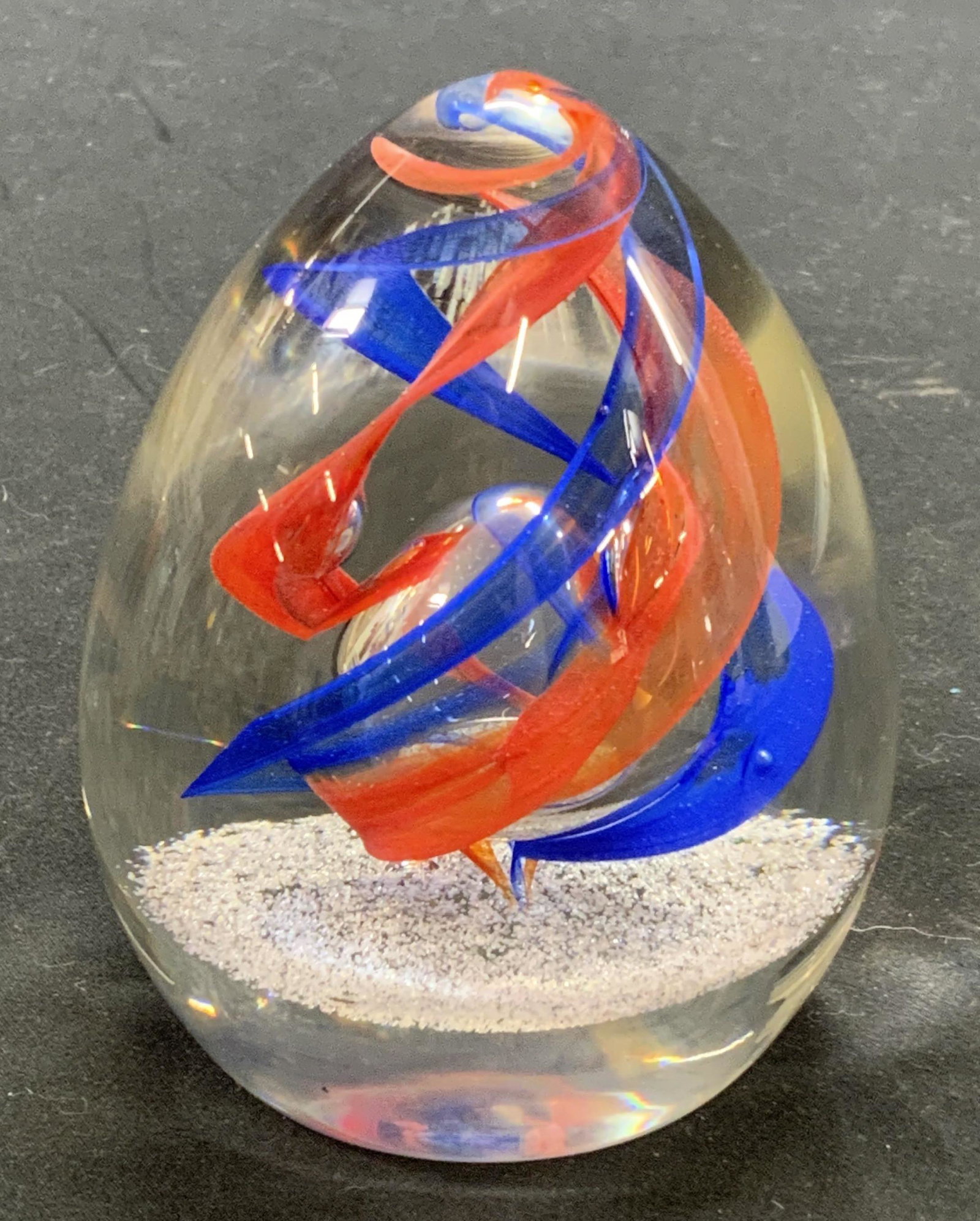 CAITHNESS MAYPOLE Collectible Glass Paperweight: CAITHNESS MAYPOLE handblown egg shaped glass paperweight with bubble detail and swirling blue and red inclusions. Measures approx. 3 inches diameter and 4 inches tall. Some scratching to surface. Made