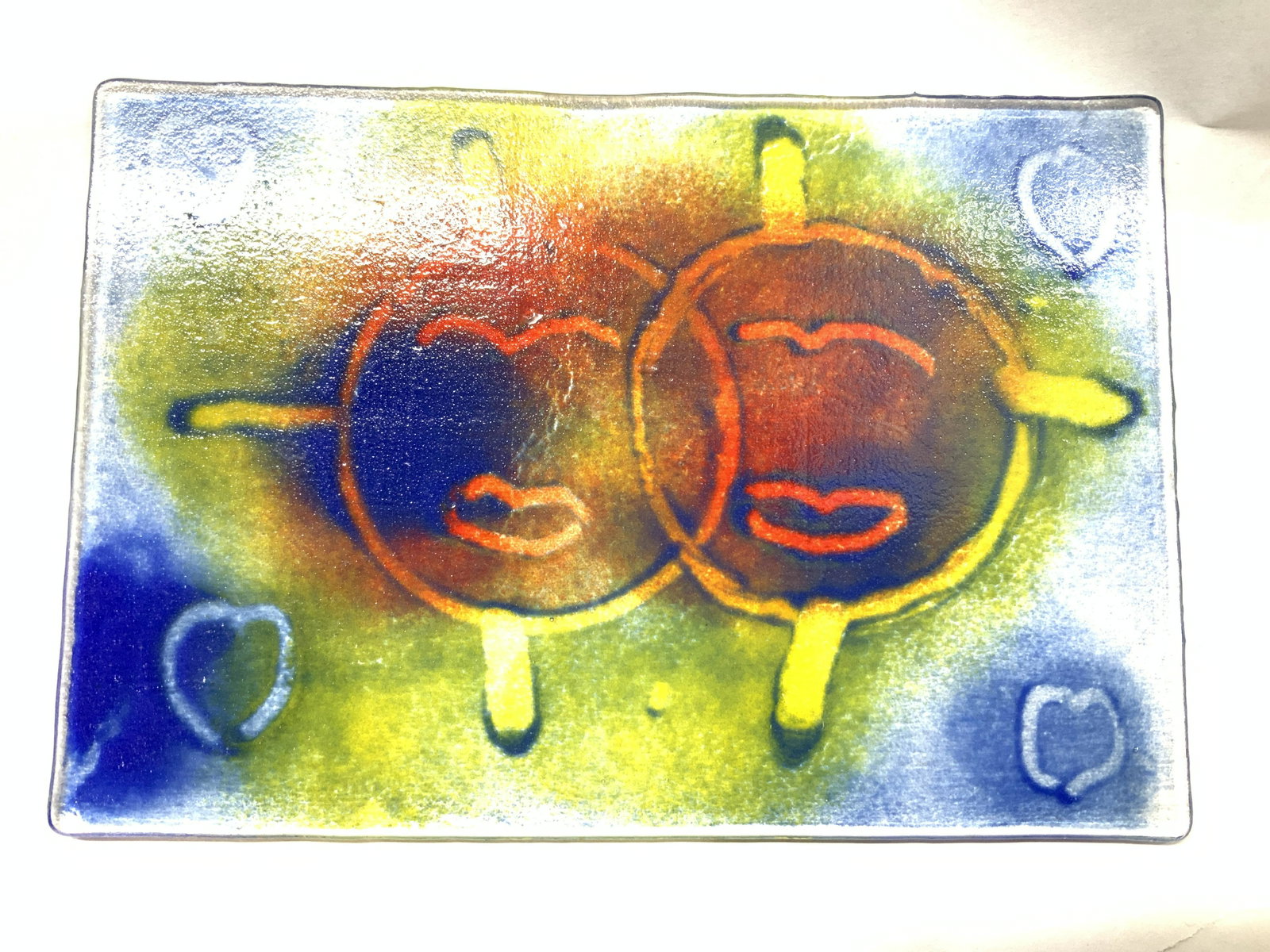 Hand Formed Glass Plate with Faces: 7 7/8 x 5.5 in. Glass Art, one side textured, the other side smooth. Two primitive abstract faces appear in center of glass , colors used are yellow, blue and red. Glass Art, Hand Formed Glass, Wall D