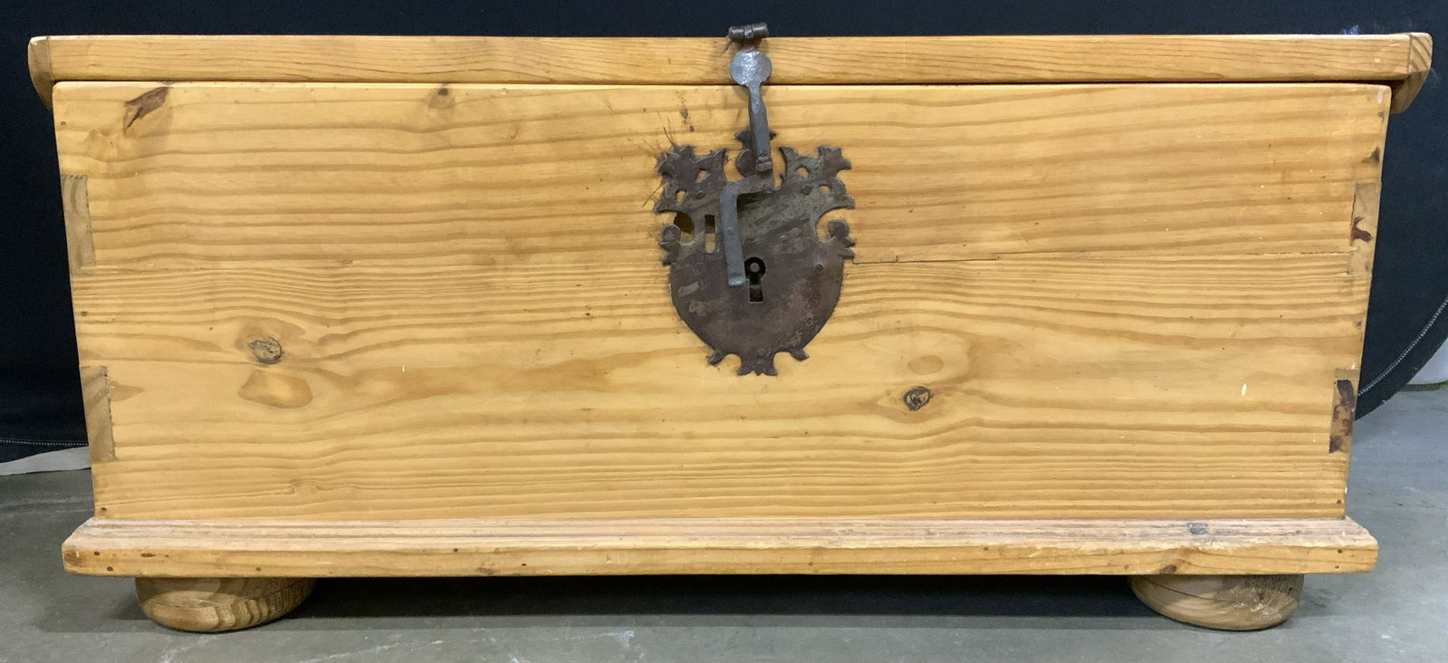 Antique Hinged Lid Wooden Chest: Chest is antique and wooden. Piece has tan tone. Chest appears to possibly be hand crafted. Piece has carved wooden feet. Lock area has metal crest structure. Chest has metal handle on each side. Incl