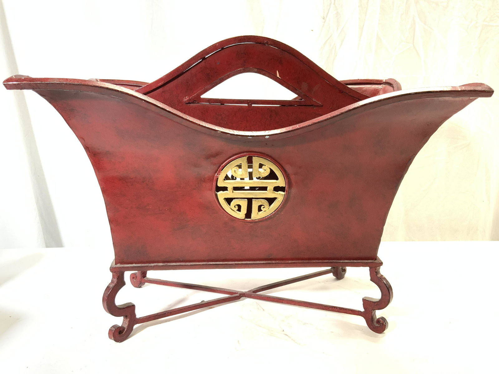 Red Asian Footed Metal Canterbury: Canterbury is red with gold toned medallion detail on sides. Piece has handle in center, and 4 curled feet with x shaped stretcher in between. Canterbury measures approx 16.5 inches tall 20.5 inches l
