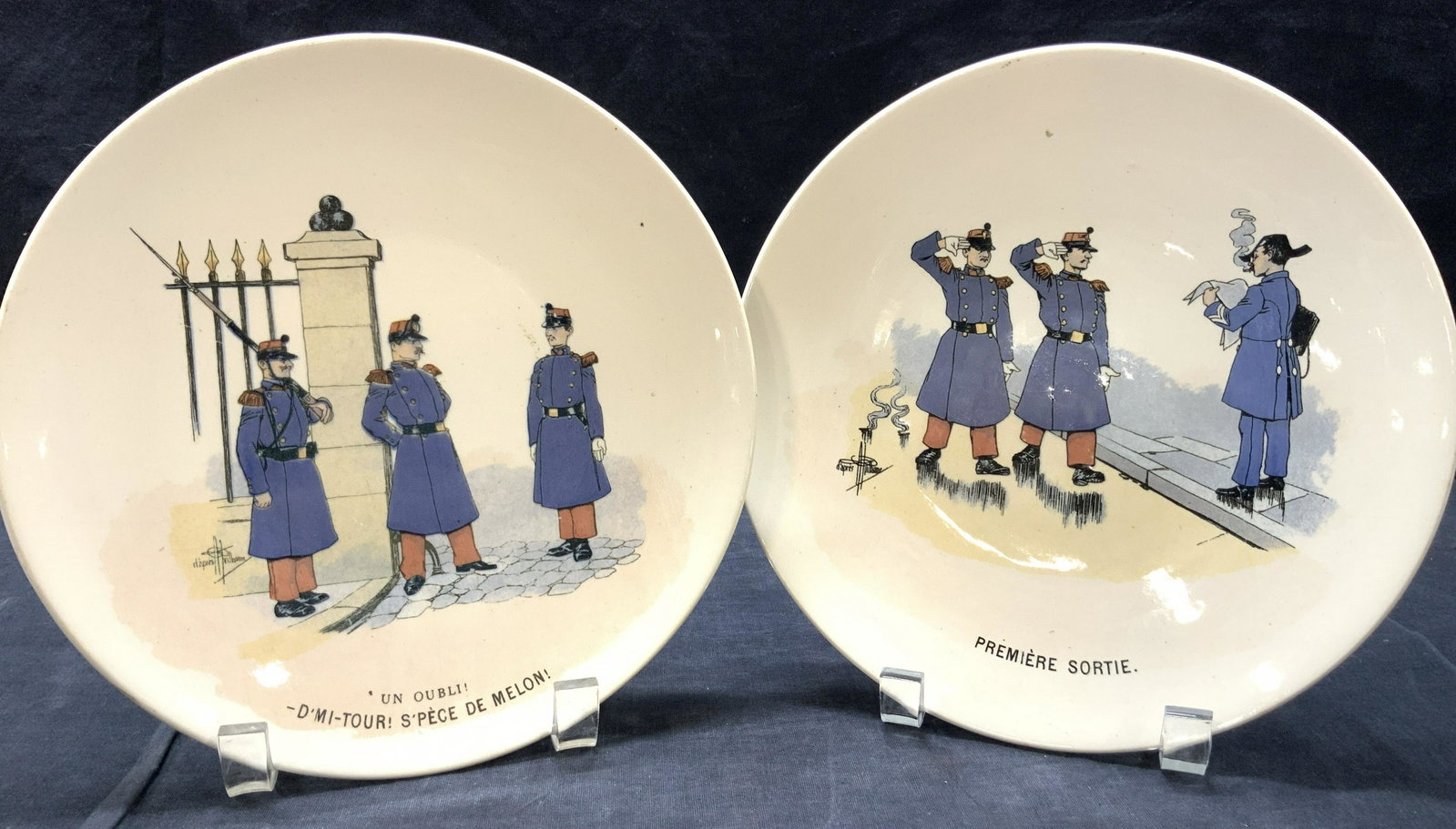 Pair Sarreguemines France Illustrated Plates: 2 porcelain illustrated plates. All marked on underside Mon Regiment Fayenceries, de Sarregeumines France. 1 plate depicts 2 soldiers saluting and walking past a smoking man with the caption on the pl