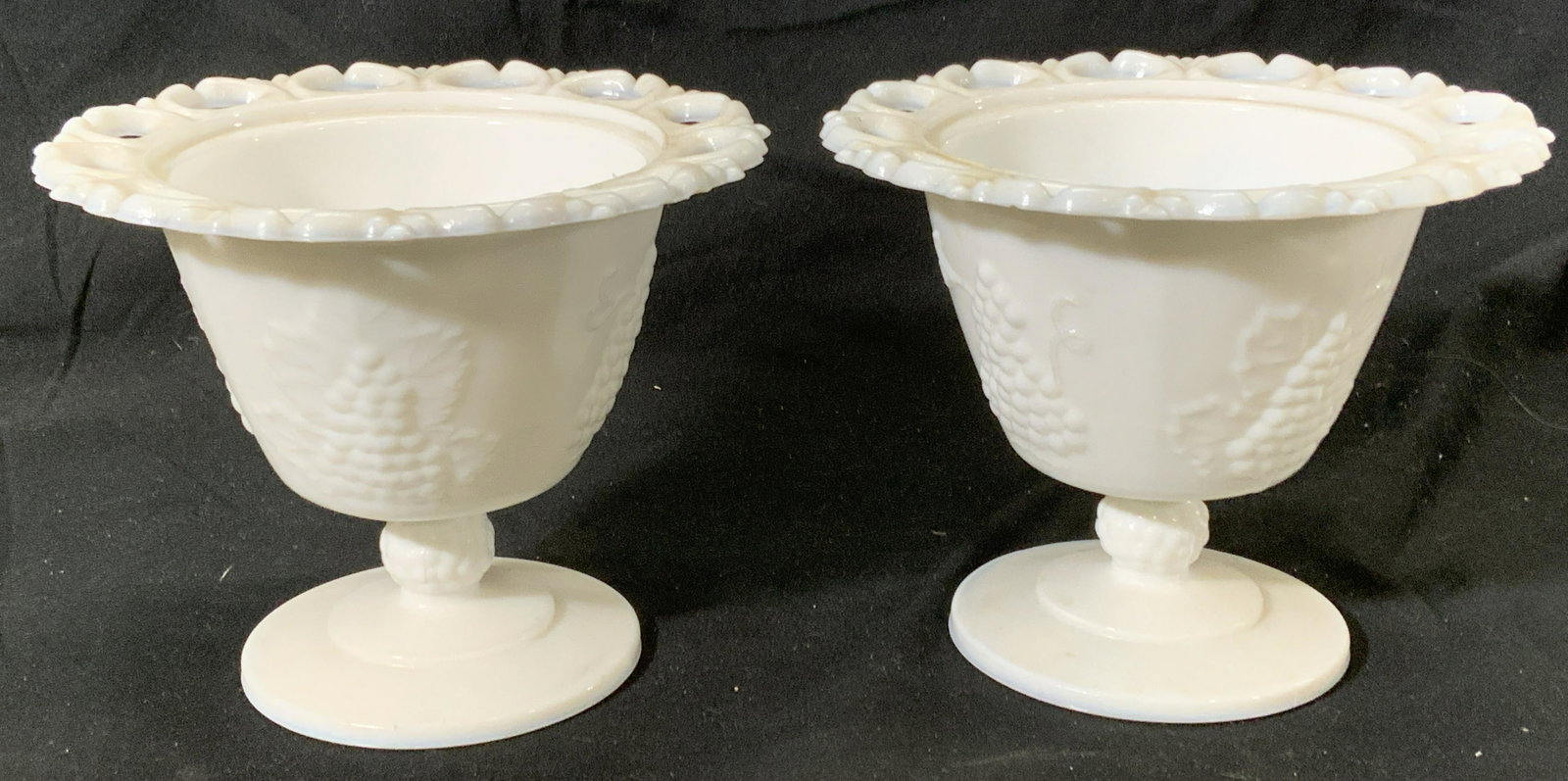 Pair Milk Glass Footed Grape Motif Vessels: Pair of milk glass footed vessels with grape motif. Measure approx. 6 diameter x 4.75 inches tall each. Some wear to surface consistent with age and exposure. Milk glass, glass vessel, glasswork, grap