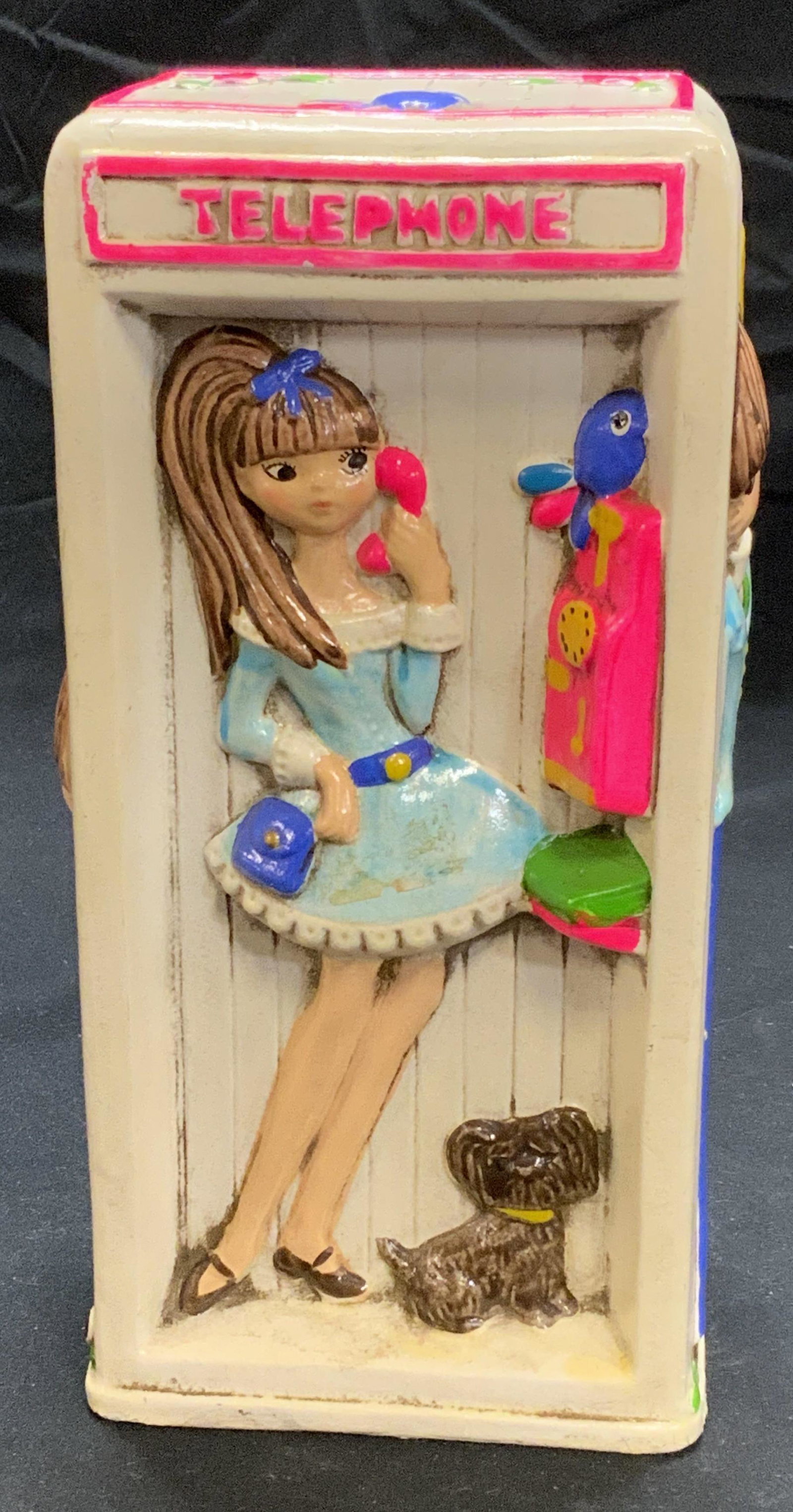 Vintage Phone Booth Coin Bank: A vintage coin bank with phone booth motif. Features male and female figures. Painted plaster. Surface wear consistent with age and exposure. Missing stopper to underside. Measures approx. 3.5 x 2.75 