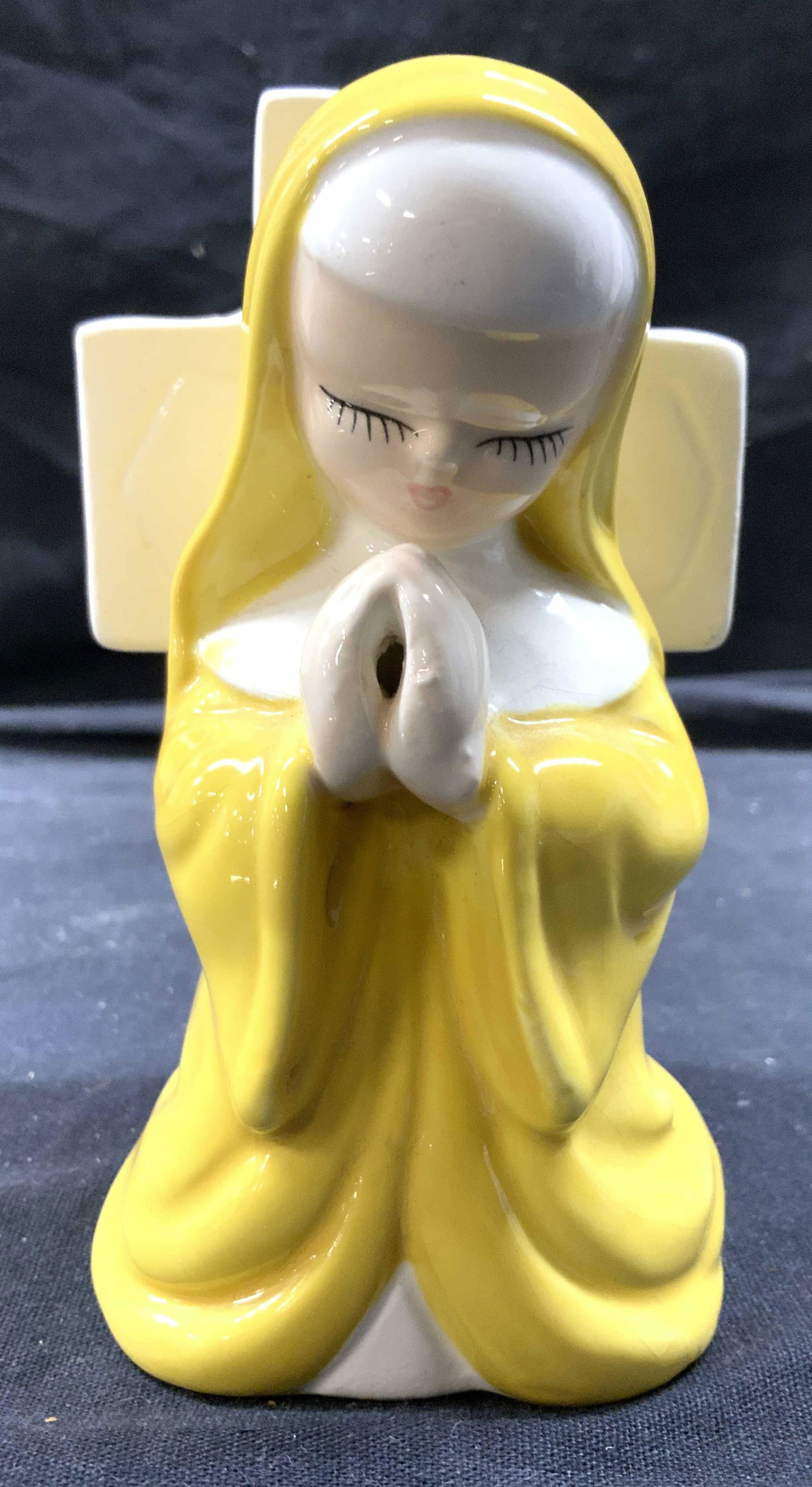 Vintage Porcelain Nun Wall Pocket: Wall pocket is porcelain. Piece depicts a praying nun in yellow clothing, standing in front of a cross. Piece is possibly hand painted. Measures approx 5 inches tall 3 inches wide 3.25 inches deep. Wa
