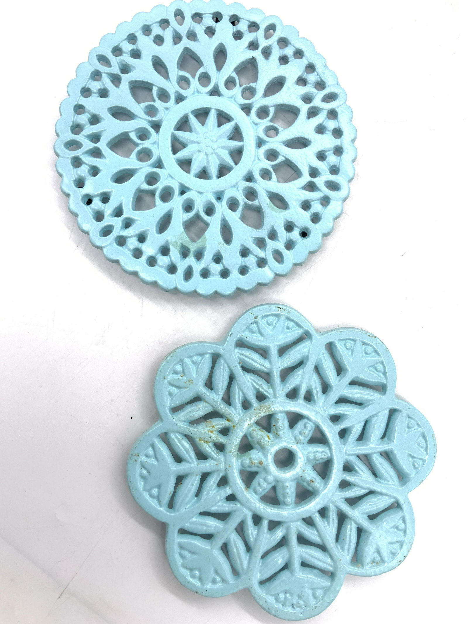 2 Vintage Painted Iron Ornate Trivets: 2 vintage blue toned painted ornate iron trivets. 1 circular with ornate cut outs with an inner Star shape, 1 snow flake inspired trivet with floral motifs. Largest is approximately 7 inch diameter. V
