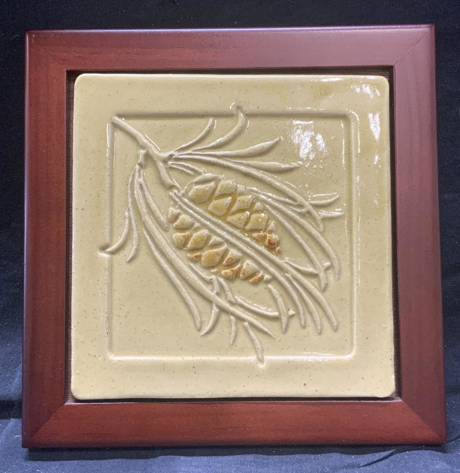 Ceramic Tile With Pine Cone Relief In Wood Frame: Ceramic Tile With Pine Cone Relief In Wood Frame, measures approx 7 3/4 x 7 3/4 in., surface wear to frame, professionally framed, not examined out of frame. Ceramic tile with pine cone relief in wood