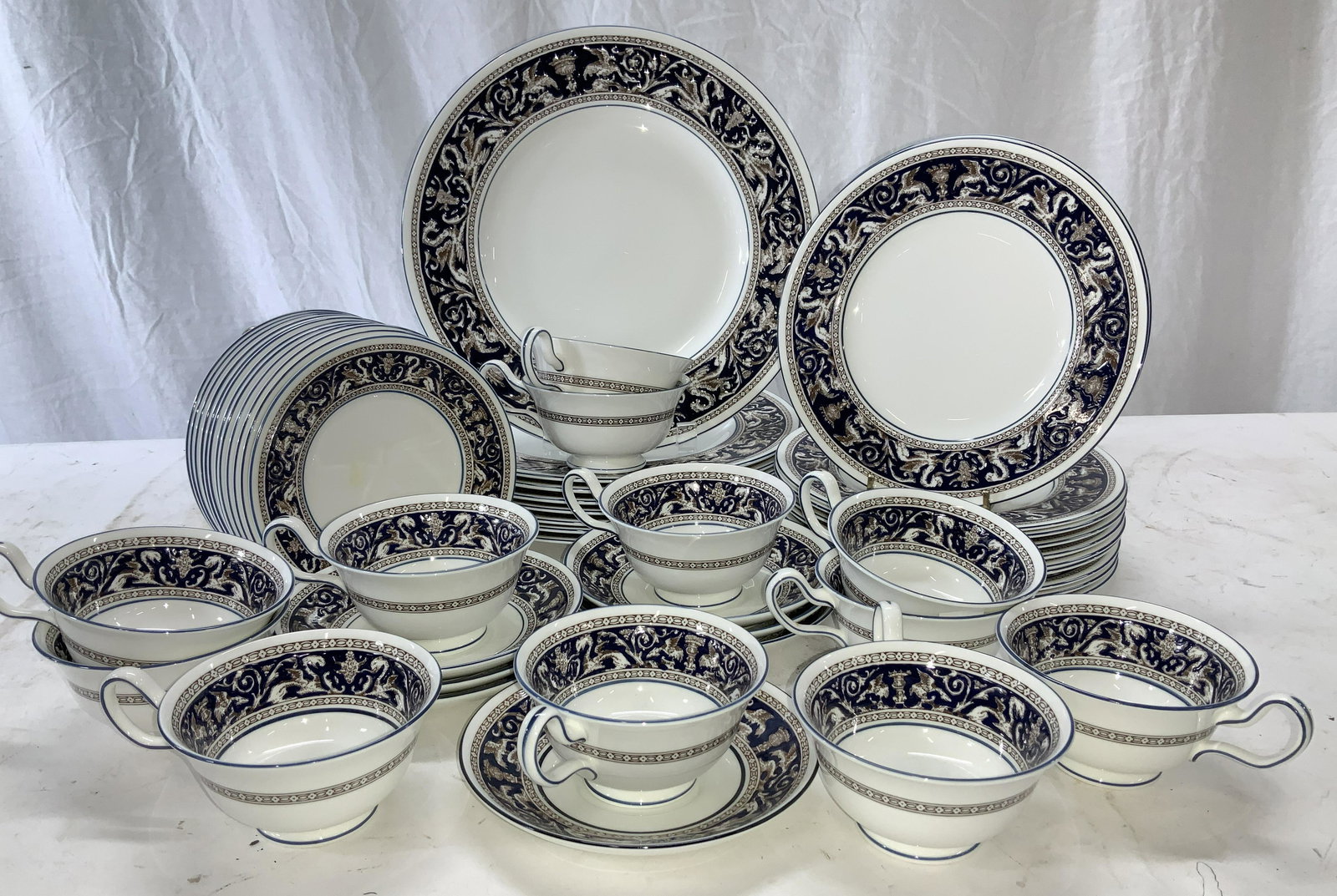 WEDGWOOD Florentine Porcelain Dinnerware 52 Eng: White porcelain chinaware set, blue rim, neoclassical Florentine embossed border in blue, chocolate an white, depicts urns, scrolls , and mythical creatures. Hallmarked with modern Wedgwood urn and si