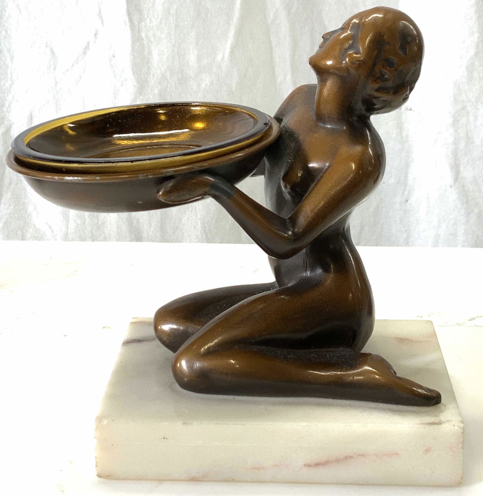Frankart Style Art Decor Nude Bronzed Statuette: Bronze toned coating over metal in FRANKART SPELTER Style. Art Deco nude kneeling lady holding an object ( originally used as an ashtray) with amber toned glass liner. Statuette sits on a marble stand