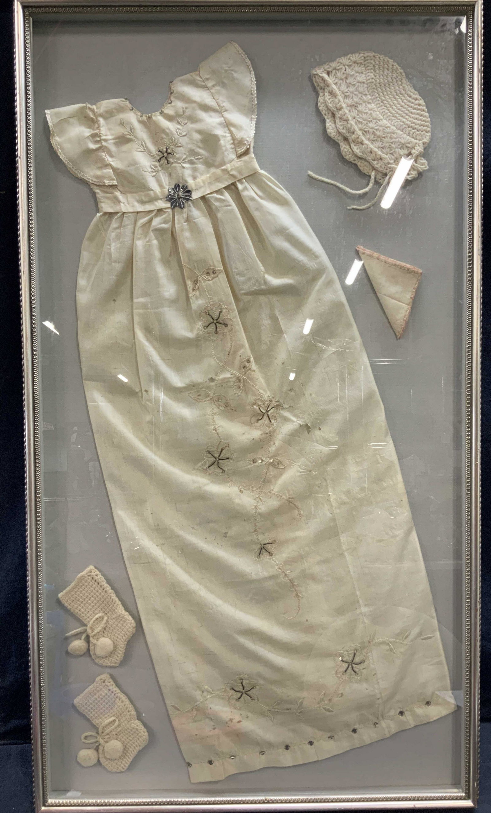 Vintage XL Framed Victorian Childs Christening Outfit: A vintage framed childs Christening outfit complete with bonnet, gown handkerchief and booties. Frame is silver toned composite made with ornate ruffled rims and braided like edges. Measures 42 x 24. 