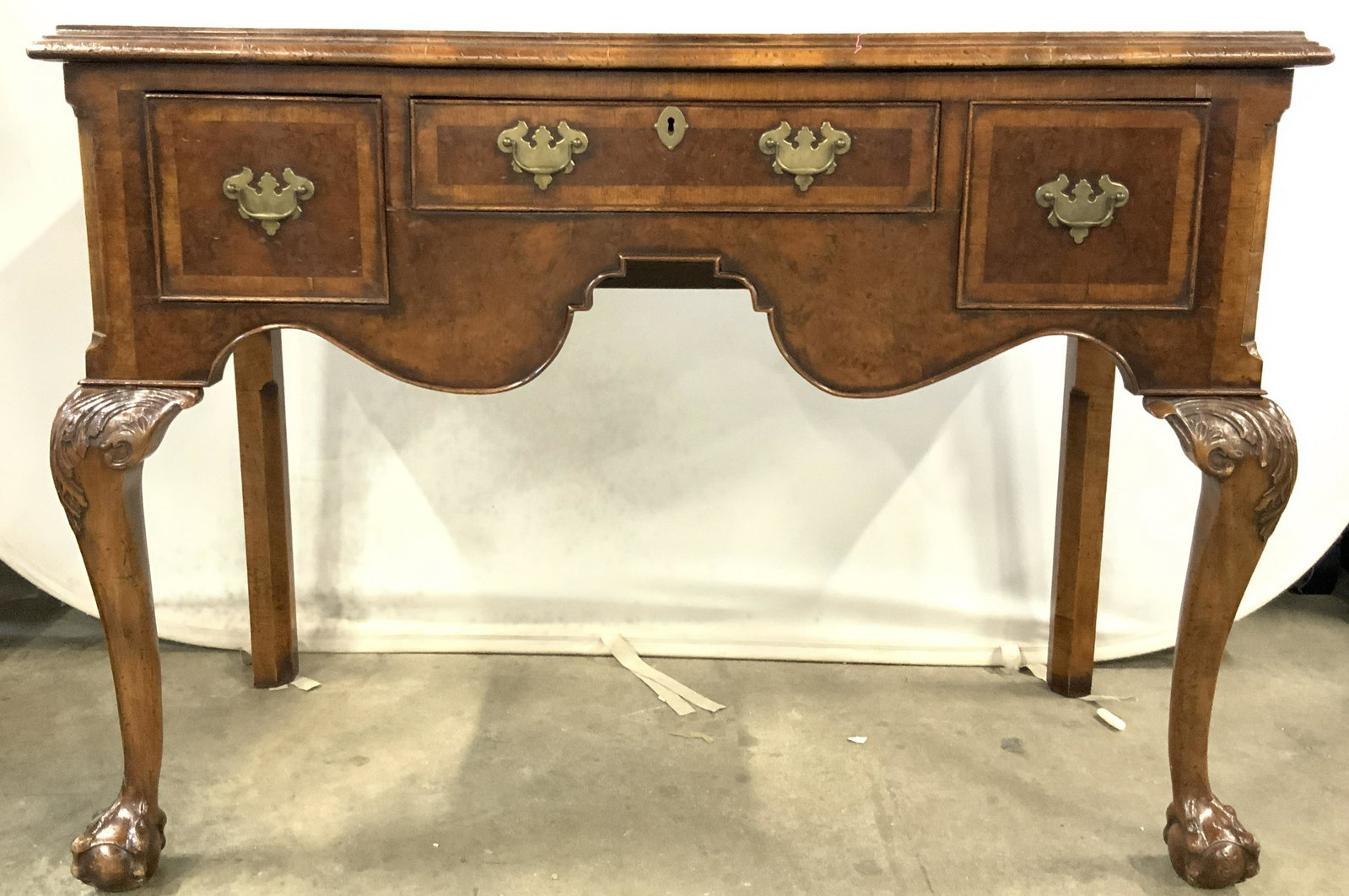 Antique Burl Wood Desk: Possibly antique wooden desk with intricately carved feather knees, claw and ball feet with antique burl wood top and double geometric banding around burl wood top. Three front facing drawers with bra