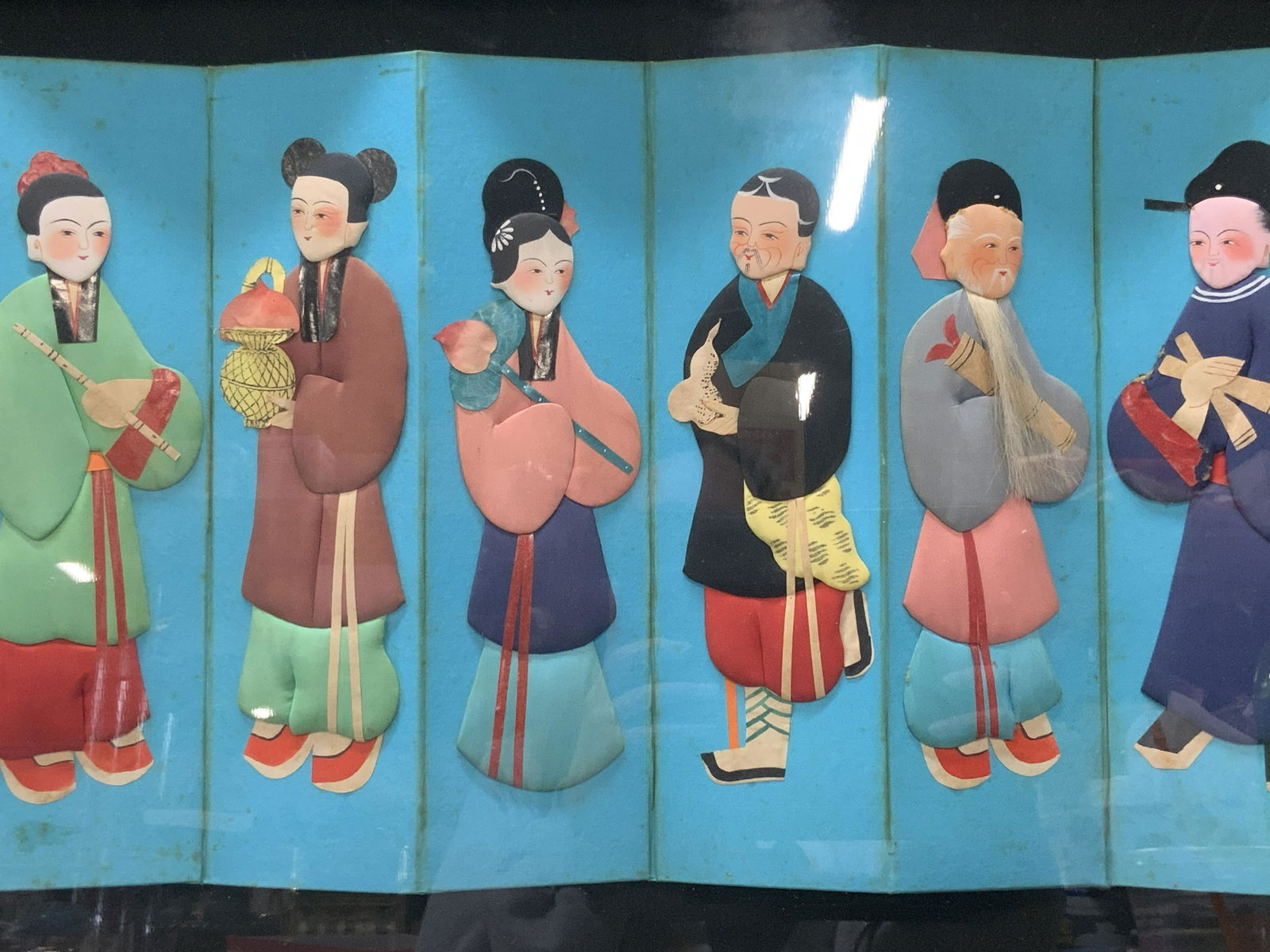 Mixed Media Asian Folded Screen Figures Collage: Mixed Media Asian Folded Screen Figures Collage, no apparent inscriptions, mixed media figures on folded turquoise screen, in frame measures approx 17 x 32 in. Gold toned wood frame, surface wear to f