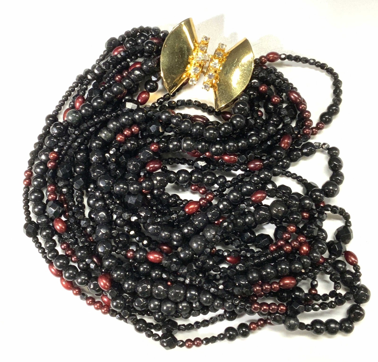 Vintage Multi Strand Black Crystal Choker Necklace: A vintage multi strand necklace with black and colorless faceted crystals and maroon beads. Gold tone box clasp. Measures approx. 17.5 inches long. Some surface wear consistent with age and exposure. 