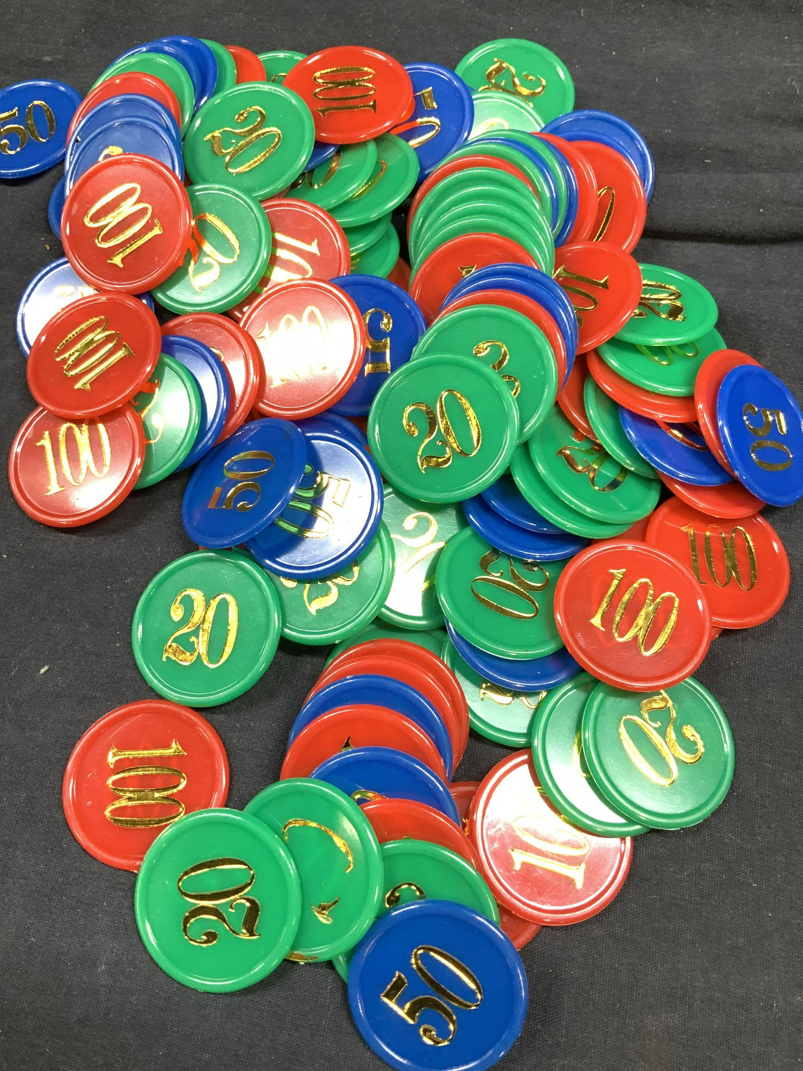 Lot of 143 Numerated Poker Chips: Red, green and blue poker chips with monetary bid numbers 20, 50 and 100. 47 Green 20 chips, 53 blue 50 chips, 43 red 100 chips. Plastic composite with gold toned paint, evident wear and losses to pai