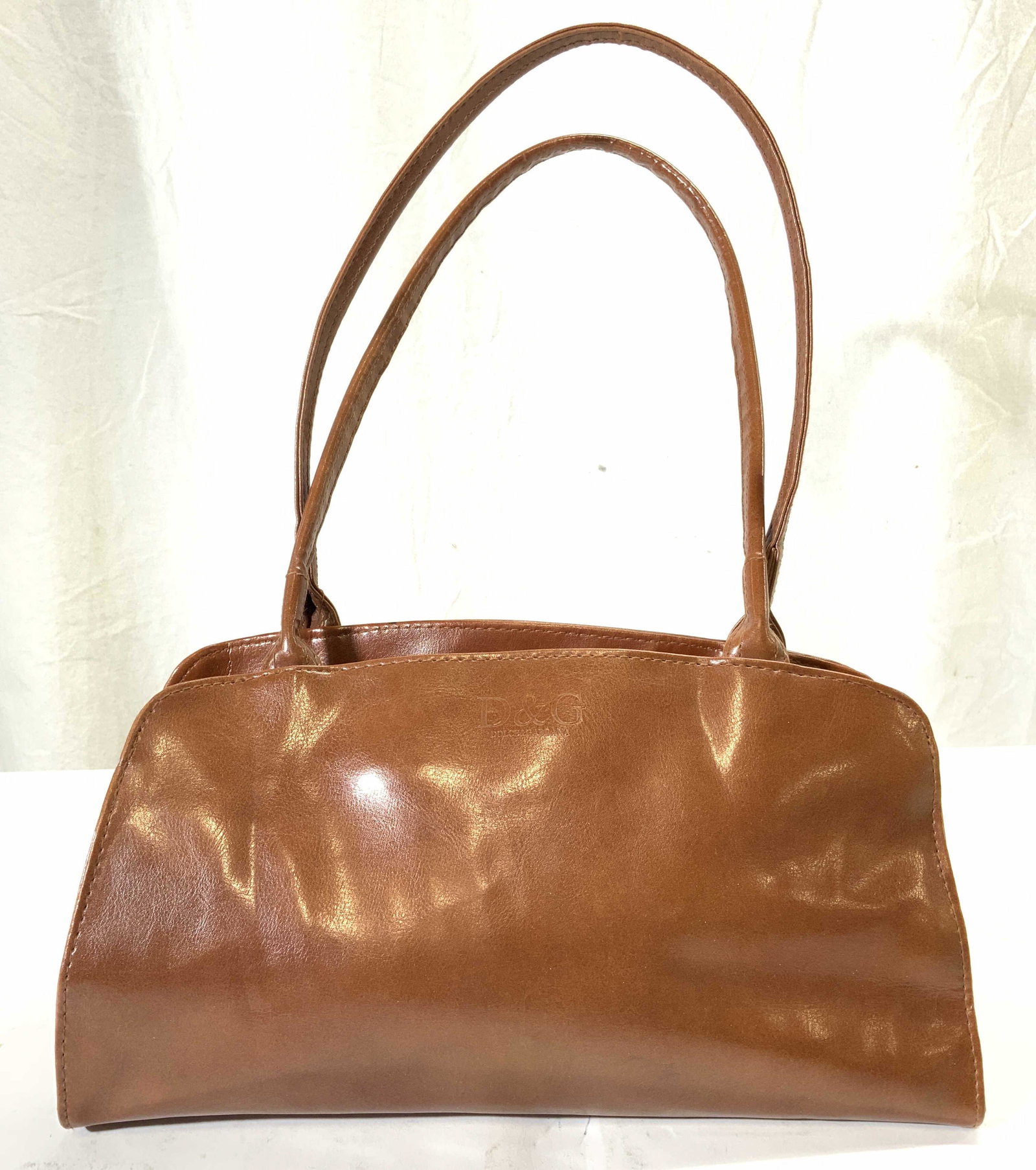 DOLCE & GABBANA Leather Purse Handbag: Front of piece is inscribed D&G DOLCE & GABBANA. Piece is light brown toned and appears to be leather. Sides have button snaps. Interior has 1 zippered pocket. Bag measures approx 17 inches tall with 