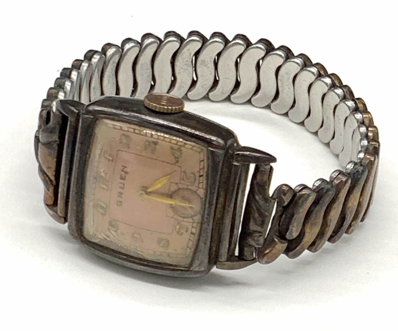 GRUEN Guildite Vintage Stretch Watch: A vintage watch. Crafted from guildite. Stretch band. Obverse reads GRUEN. Copper hue to the watch face. Reverse reads GRUEN GUILDITE BASE METAL and STAINLESS. Some cracking and discoloration present.