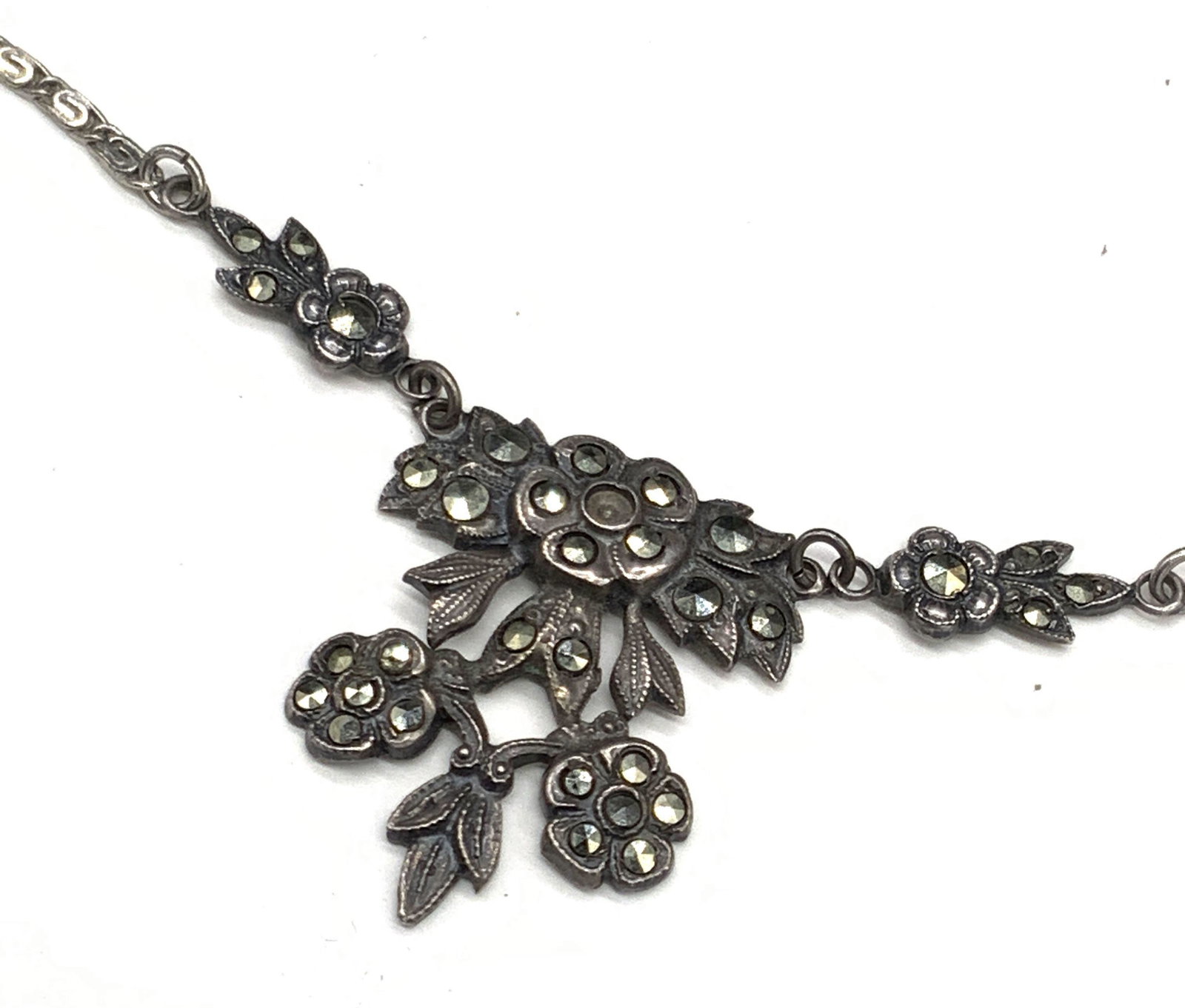 STERLING SILVER Vintage Marcasite Necklace: A sterling silver necklace featuring a floral pendant. The pendant features etched metalwork and faceted marcasite. C spring clasp marked STERLING, MANY. Pendant marked STERLING. Possibly meant to rea