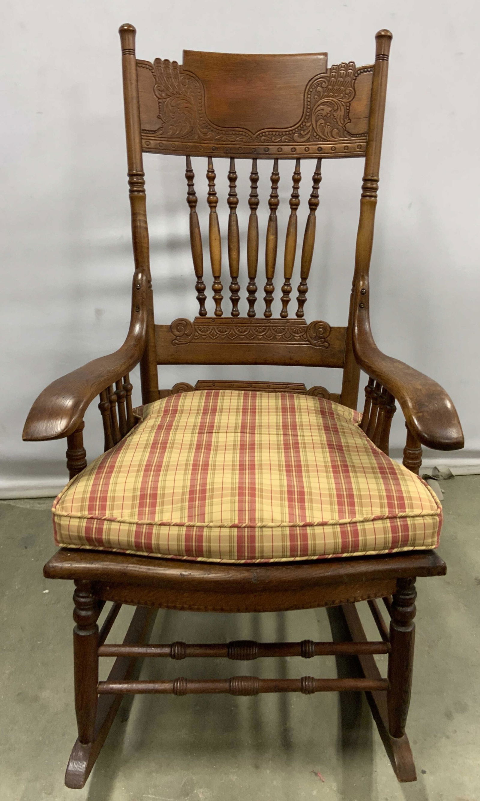 Vintage Carved & Etched Wooden Rocking Chair: A vintage wooden rocking chair with a removable cushion. The rocking chair features etched and carved woodwork. The seat of the rocking chair is caned. The back features carved wooden spindles, floral